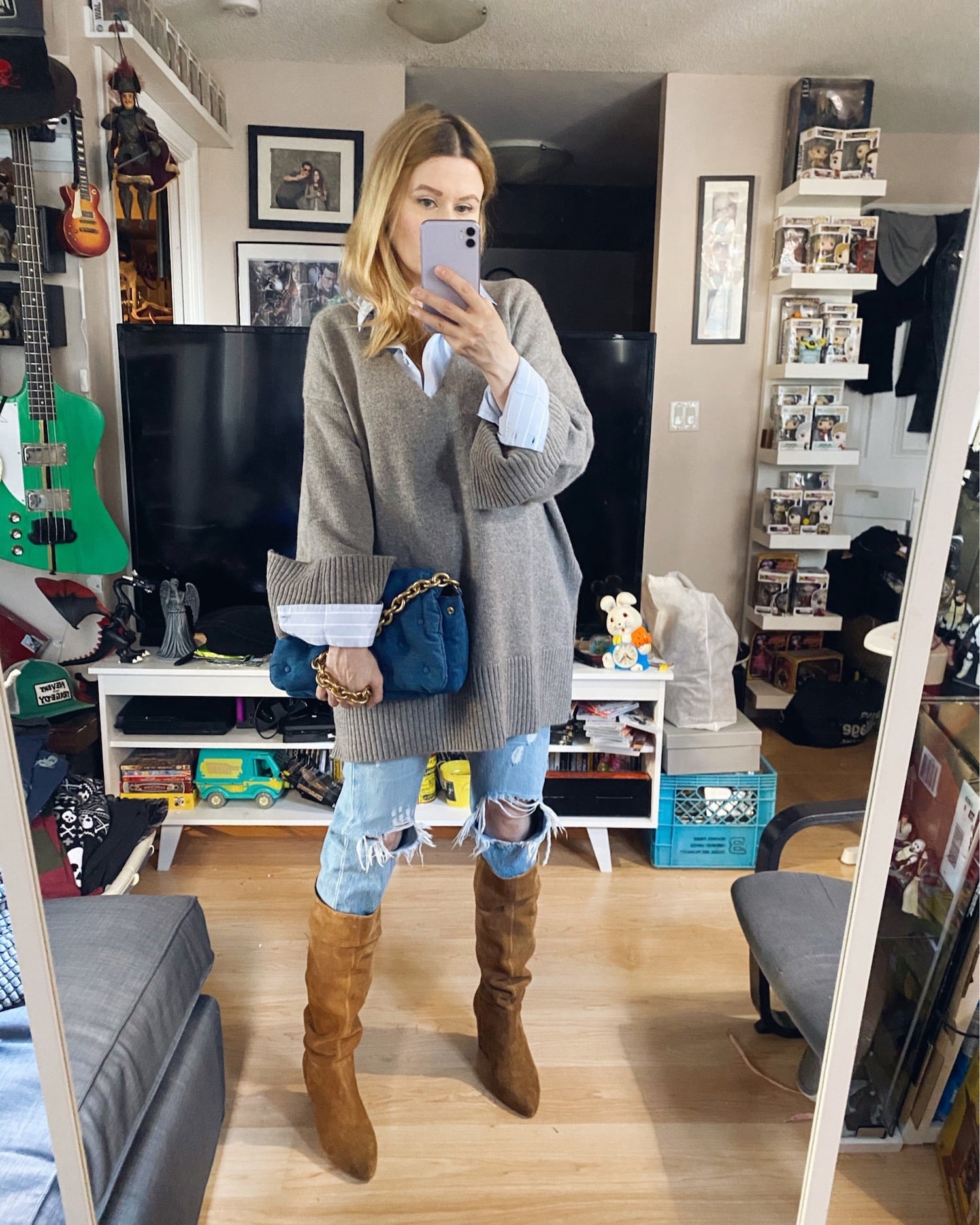 Blogger Sara Watson is wearing and oversized V-neck sweater over a blue button up, Levis 501s, and knee high cognac coloured boots.