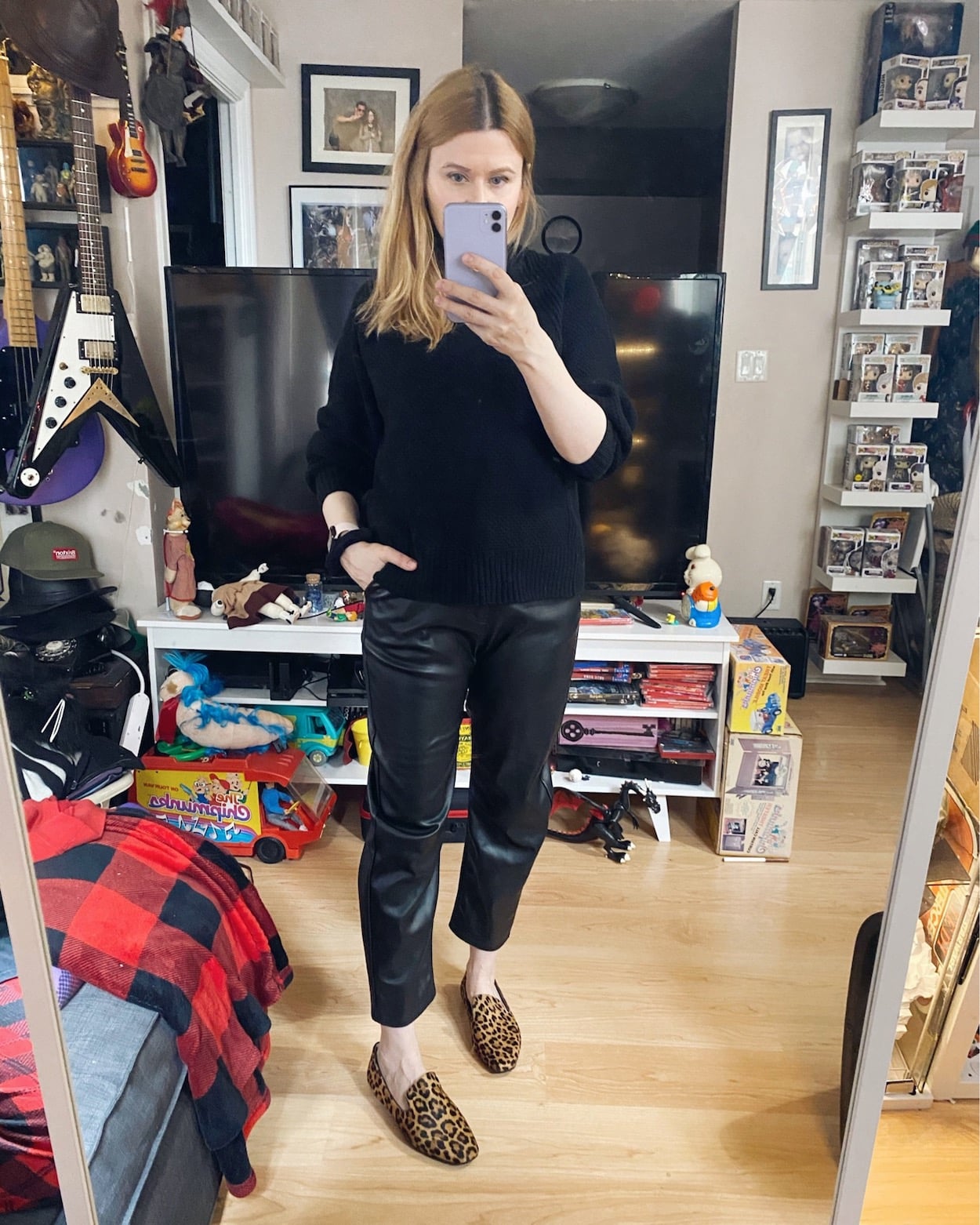 A woman is wearing a black sweater, faux leather trousers, and animal print loafers