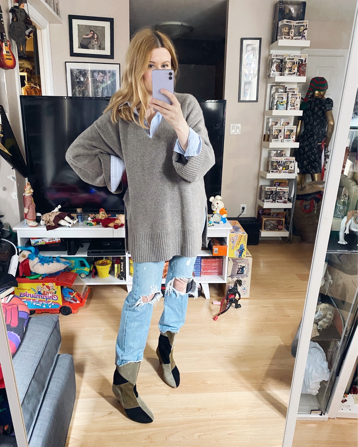 A woman is wearing a blue button up, oversized sweater, Levi's 501, and Isabel Marant boots