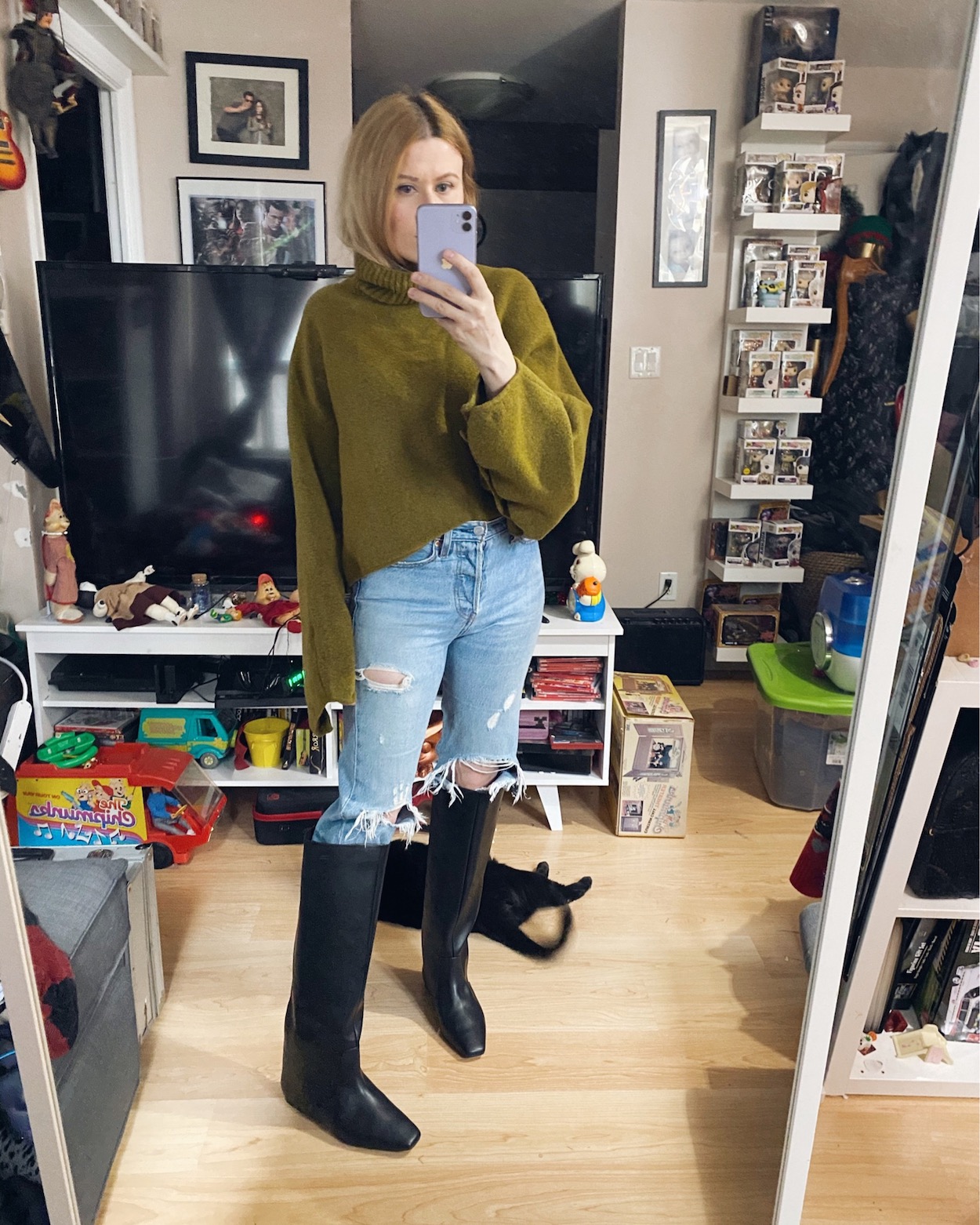 A woman is wearing a green sweater, Levi's 501s, and black knee high boots