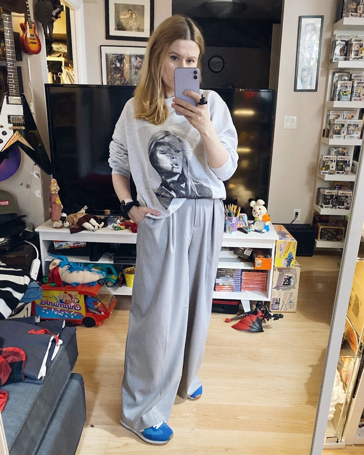 A woman is wearing an Anine Bing sweatshirt, wide leg grey trousers, and blue vejas.