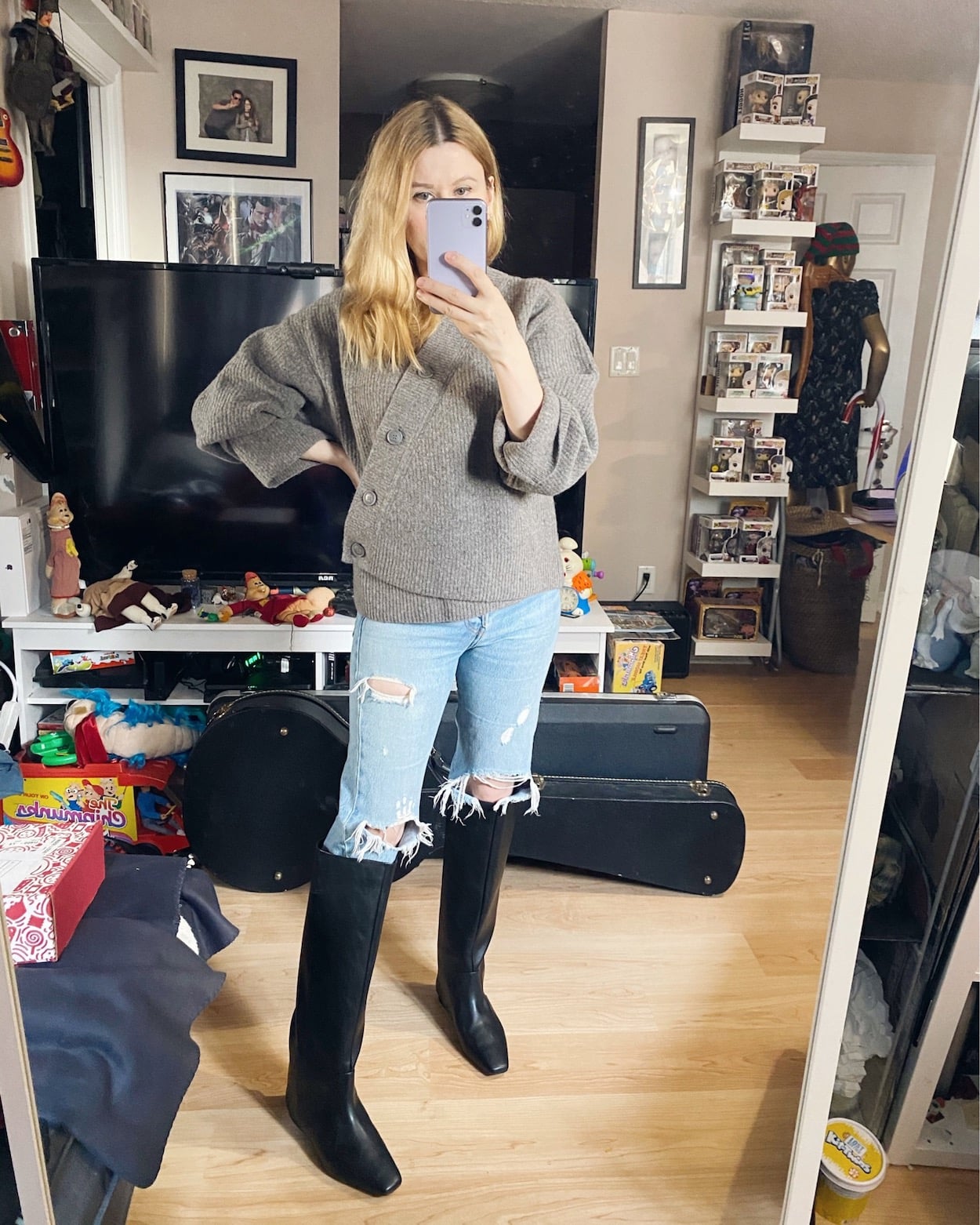 A woman is wearing an asymmetrical cardigan, Levi's 501s, and black knee high boots