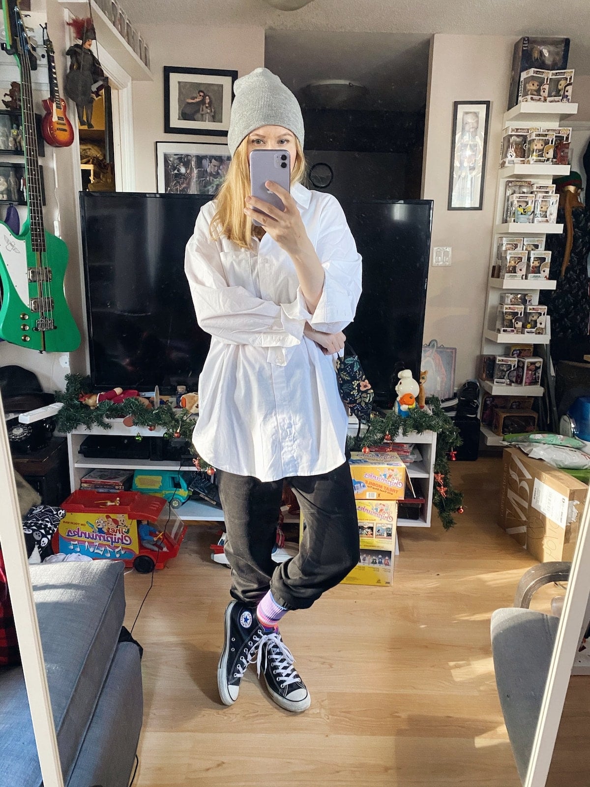 A woman wearing an oversized white blouse, joggers, Converse, and a beanie.