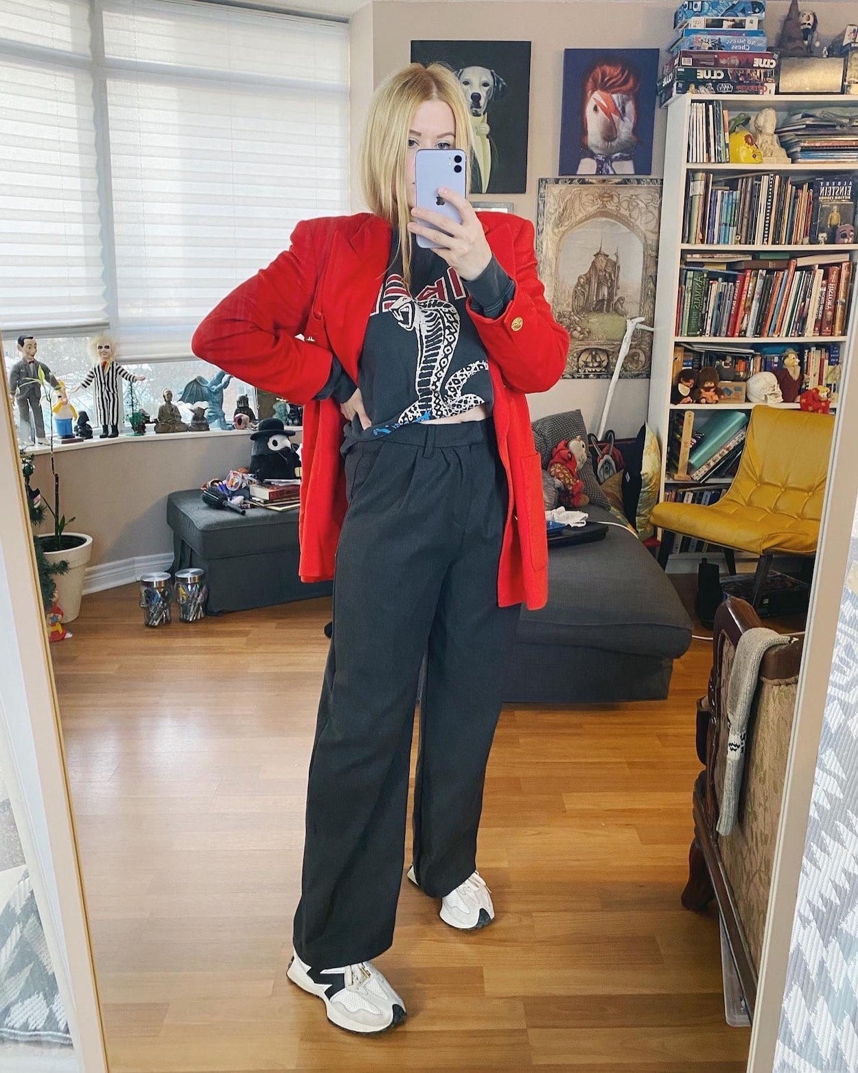 A blonde woman is wearing a bright red vintage Escada blazer, with an Anine Bing Serpent sweatshirt, grey trousers, and white New Balance Sneakers.