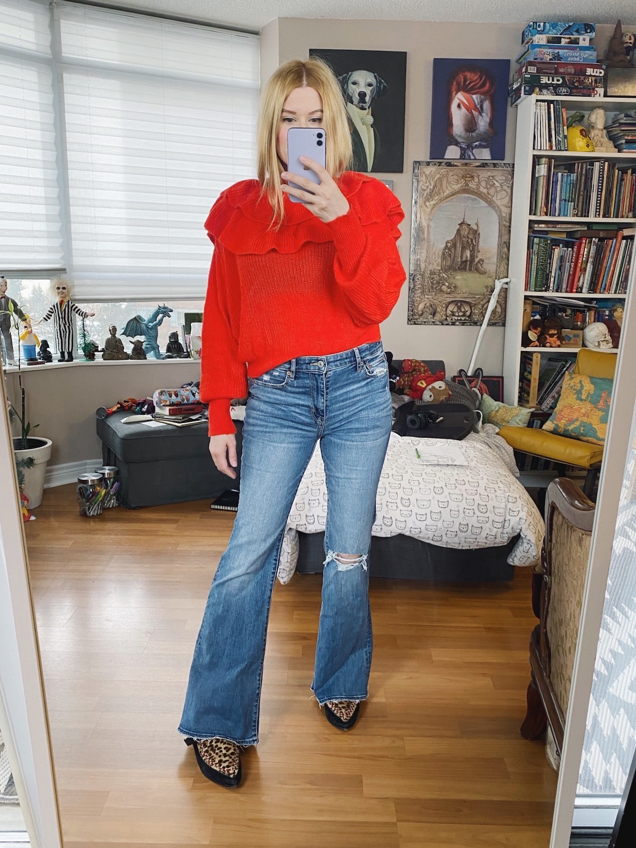 A blonde woman is wearing a bright red sweater, flare jeans, and animal print boots.