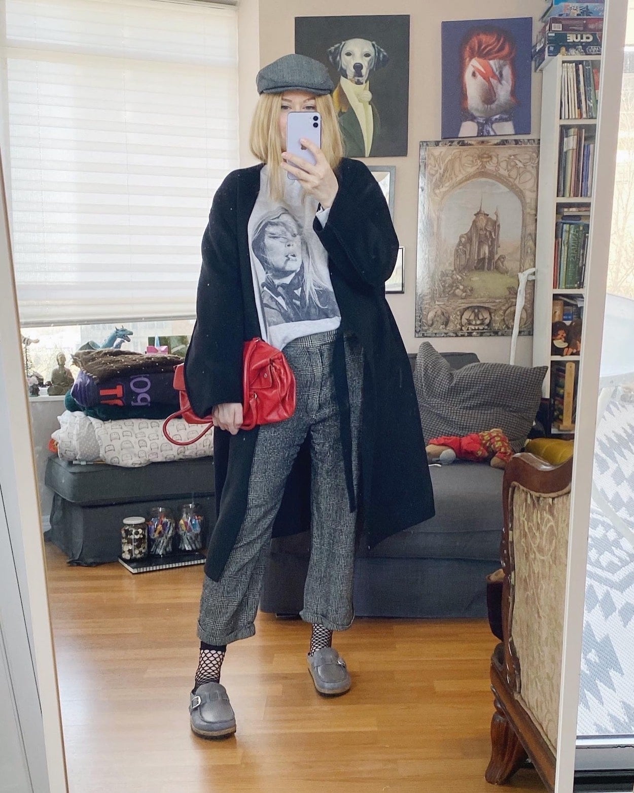 A blonde woman is wearing an Anine Bing sweatshirt, vintage trousers, a wrap coat, Birkenstocks, a newsboy cap, and a vintage prada bag.