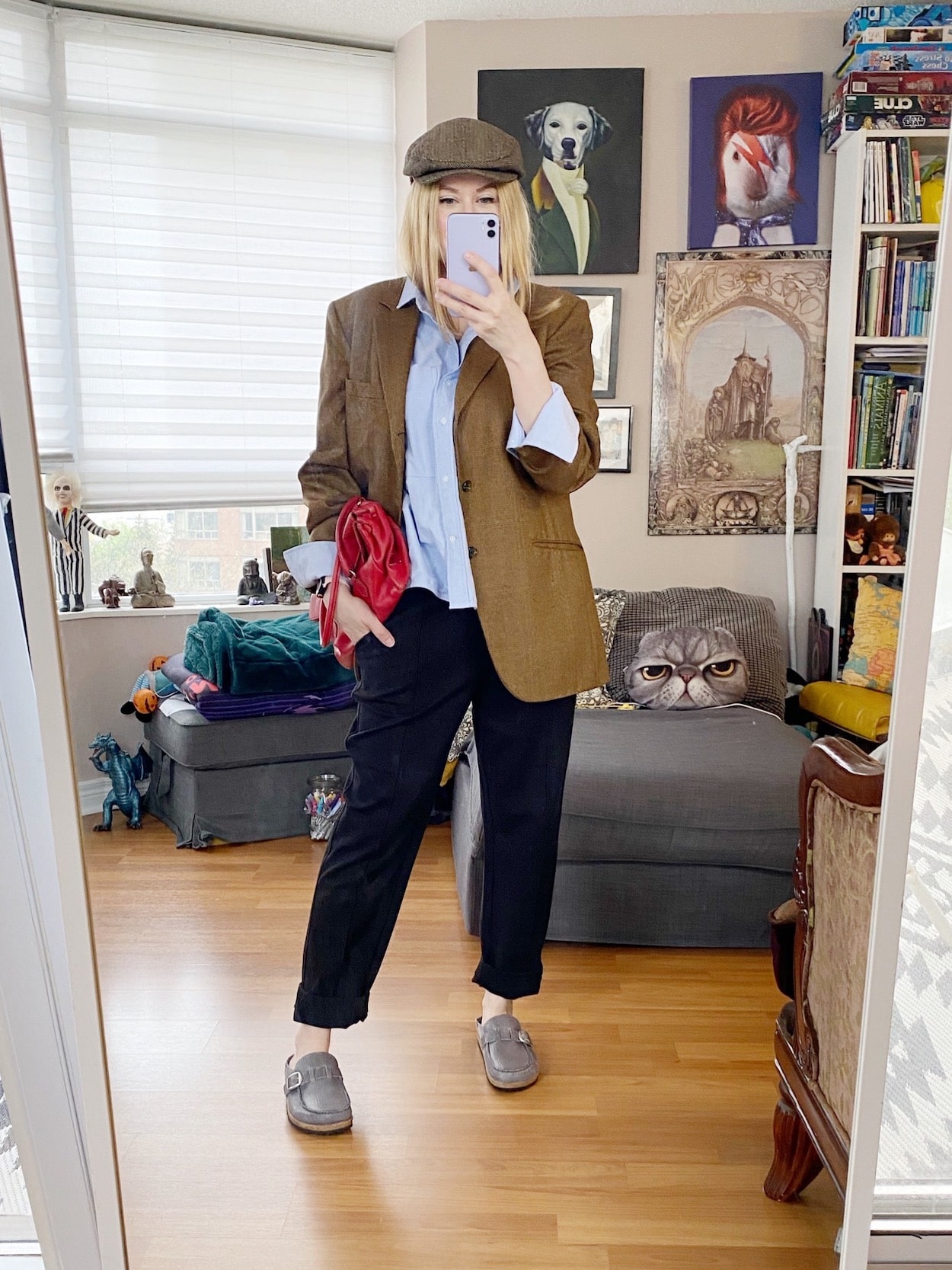 A blonde woman is wearing Everlane Dream Pants, a blue oxford, vintage blazer, newsboy cap, Birkenstocks, and a vintage Prada bag.