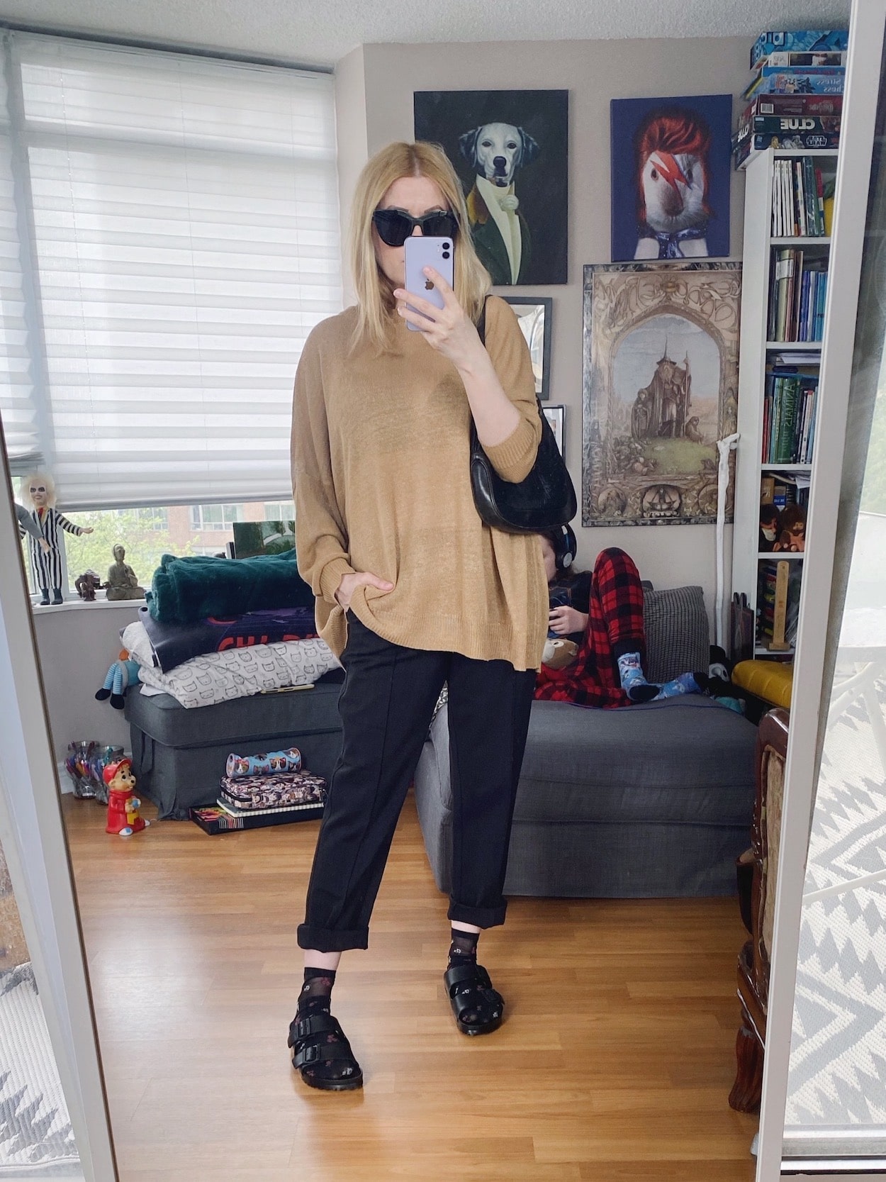 A blonde woman is wearing a camel linen sweater, black cuffed trousers, socks with Birkenstocks, black sunglasses, and a vintage Gucci Jackie bag.