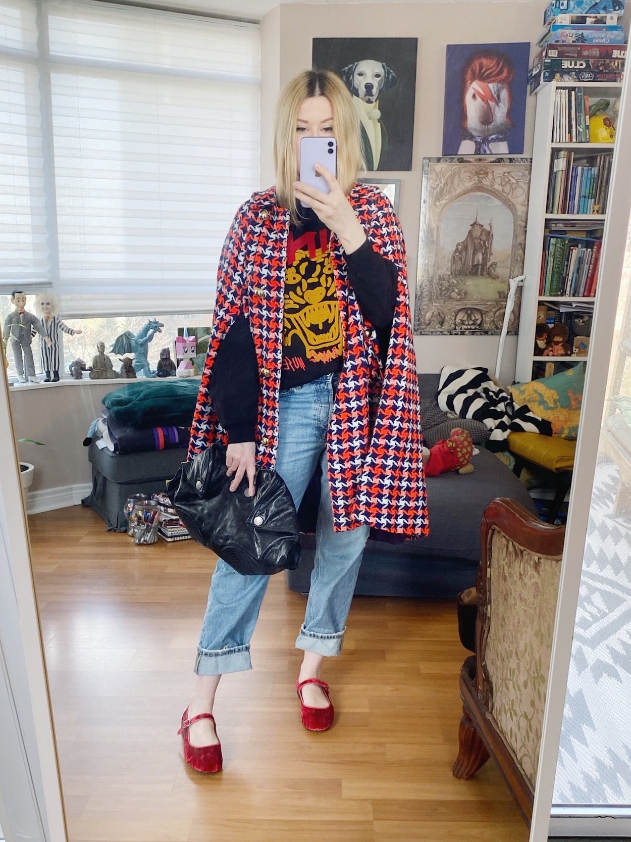 A blonde woman is wearing an Anine Bing sweatshirt, jeans, red Mary Janes, a vintage cape, and an Alexander McQueen cape.