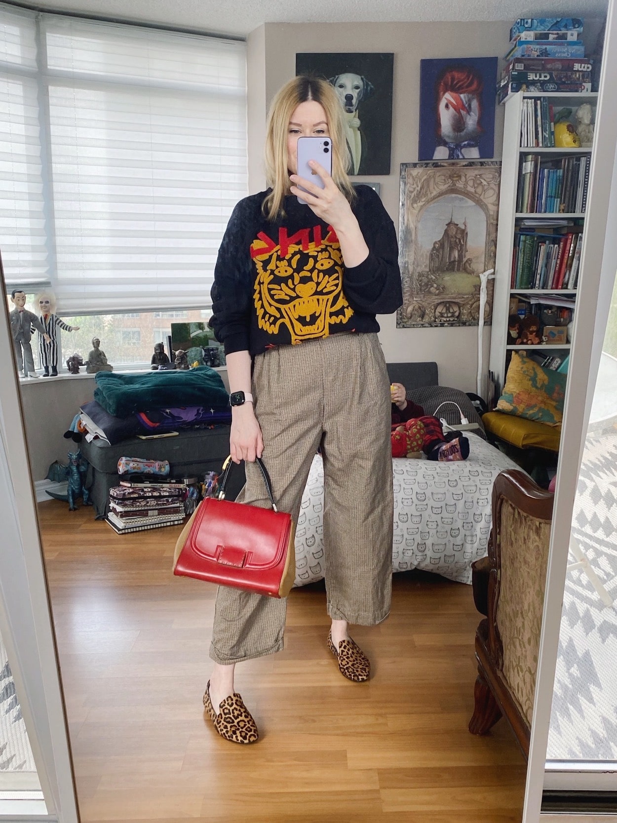 A blonde woman is wearing vintage Caliv Klein trousers, an Anine Bing sweatshirt, animal print loafers, and is carrying a Fendi bag.