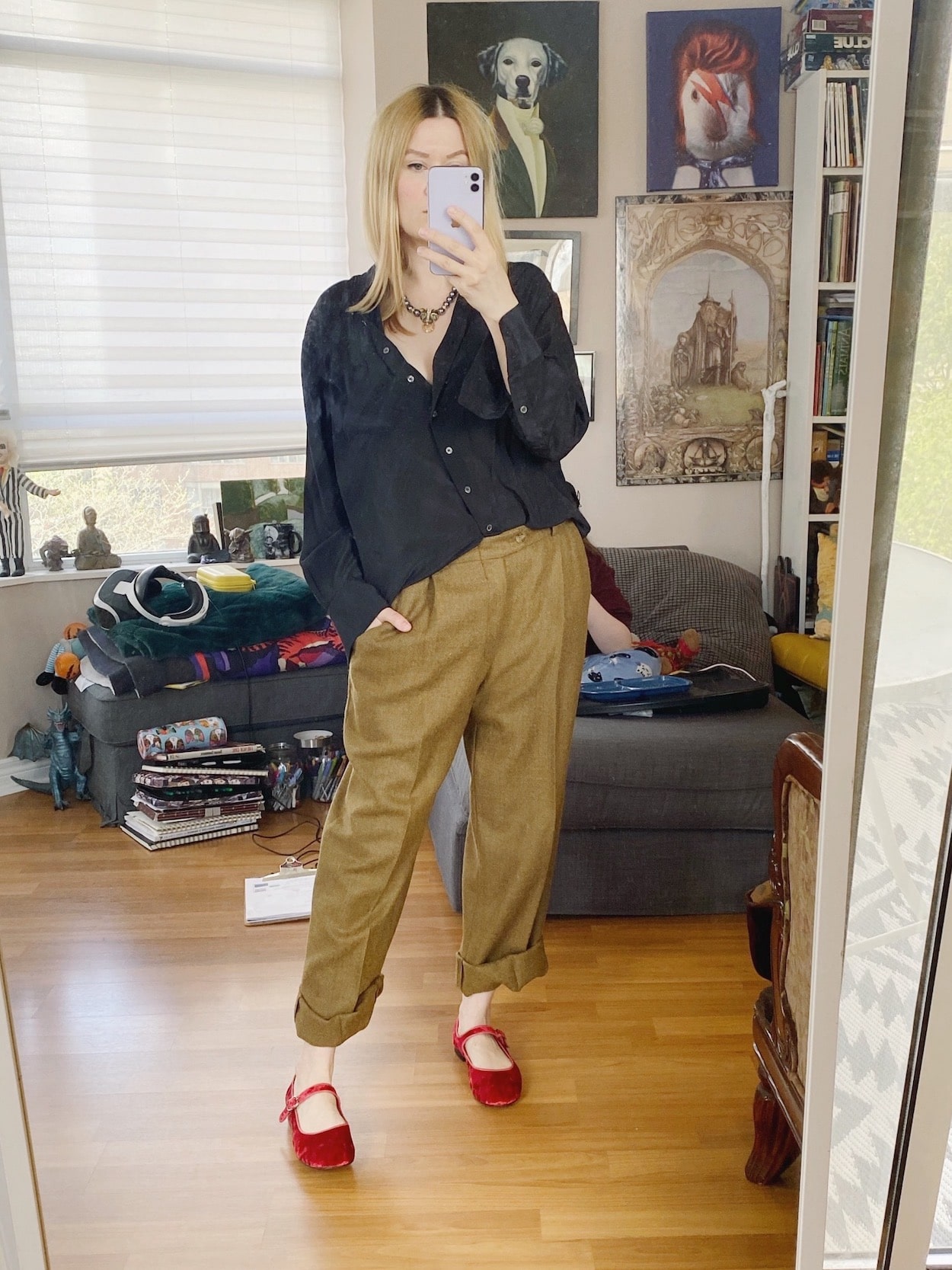 A blonde woman is wearing vintage trousers, a silk blouse, a vintage Kenneth Jay Lane necklace, and red velvet Mary Janes.