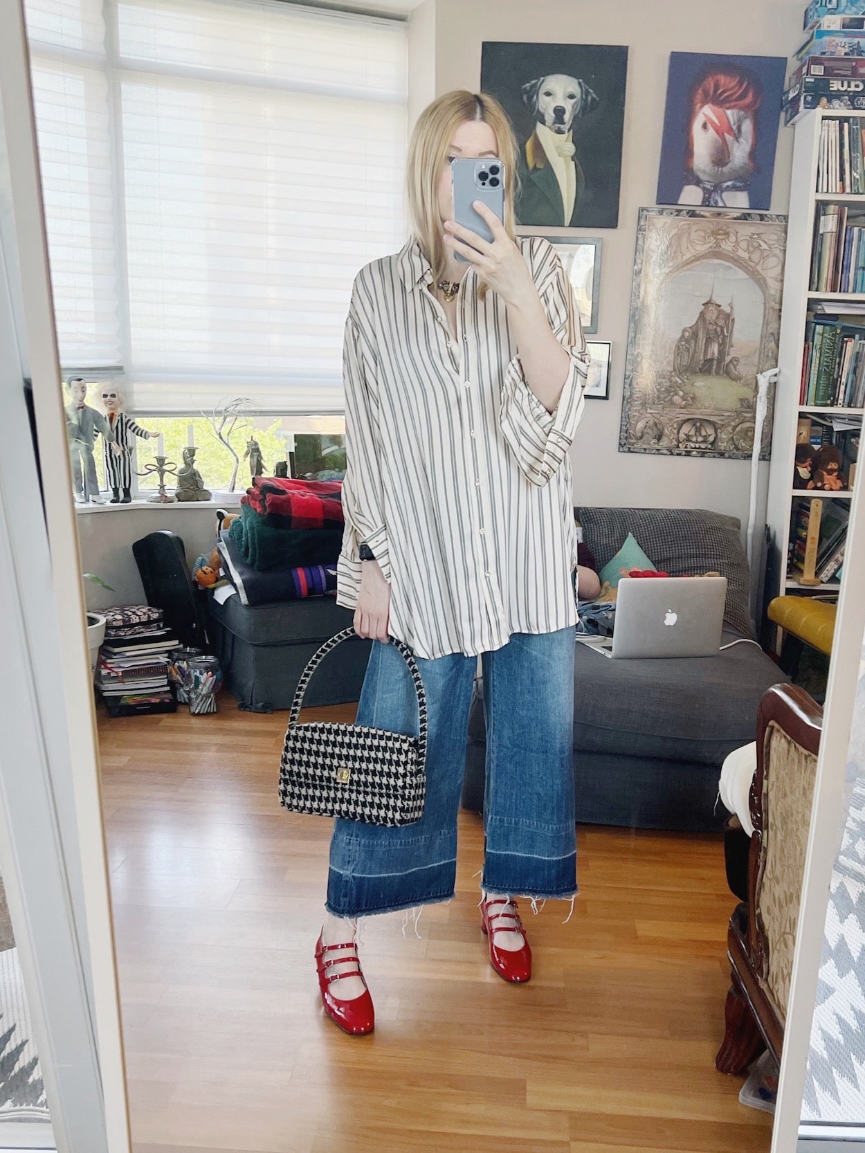 A blonde woman is wearing wide leg, cropped jeans, and oversized striped button up, a houndstooth handbag, and red mary janes.