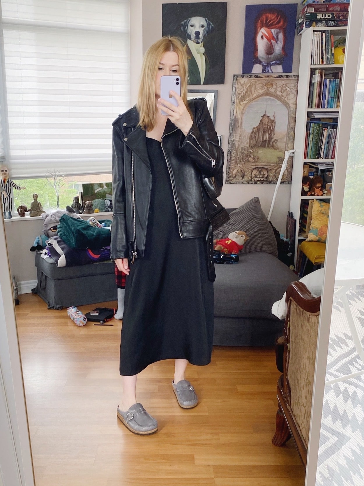 A blonde woman is wearing a black slip dress, oversized leather jacket, Birkenstock clogs, and a vintage Gucci bag.