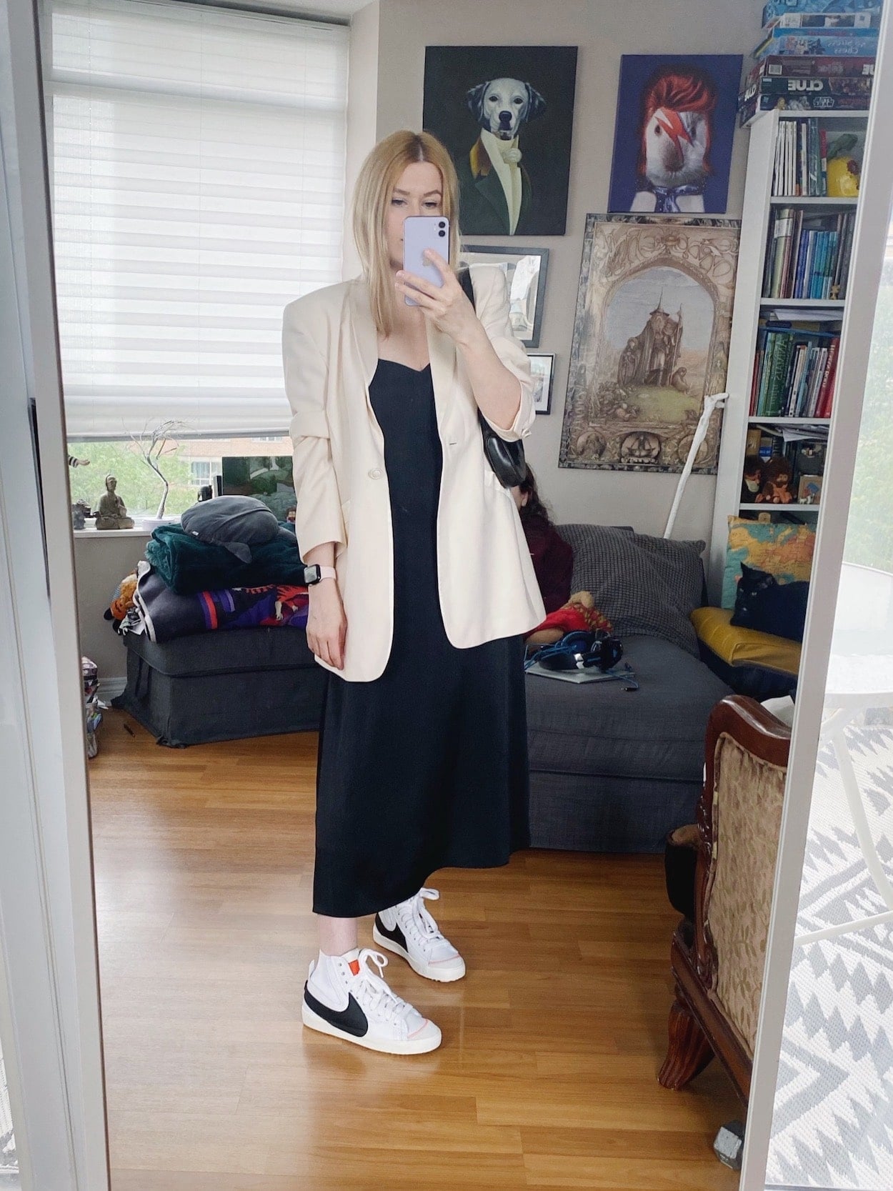 A blonde woman is wearing a black slip dress, a white vintage Escada blazer, Nike Blazers, and a vintage Gucci bag.