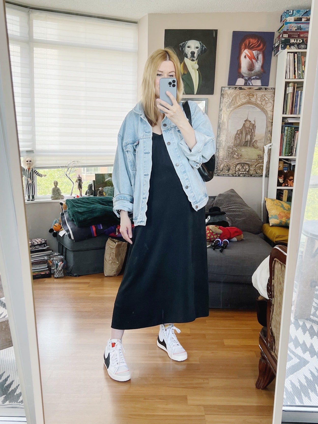 A blonde woman is wearing a black slip dress, a vintage Levi's jean jacket, a vintage Gucci bag, and Nike Blazers.