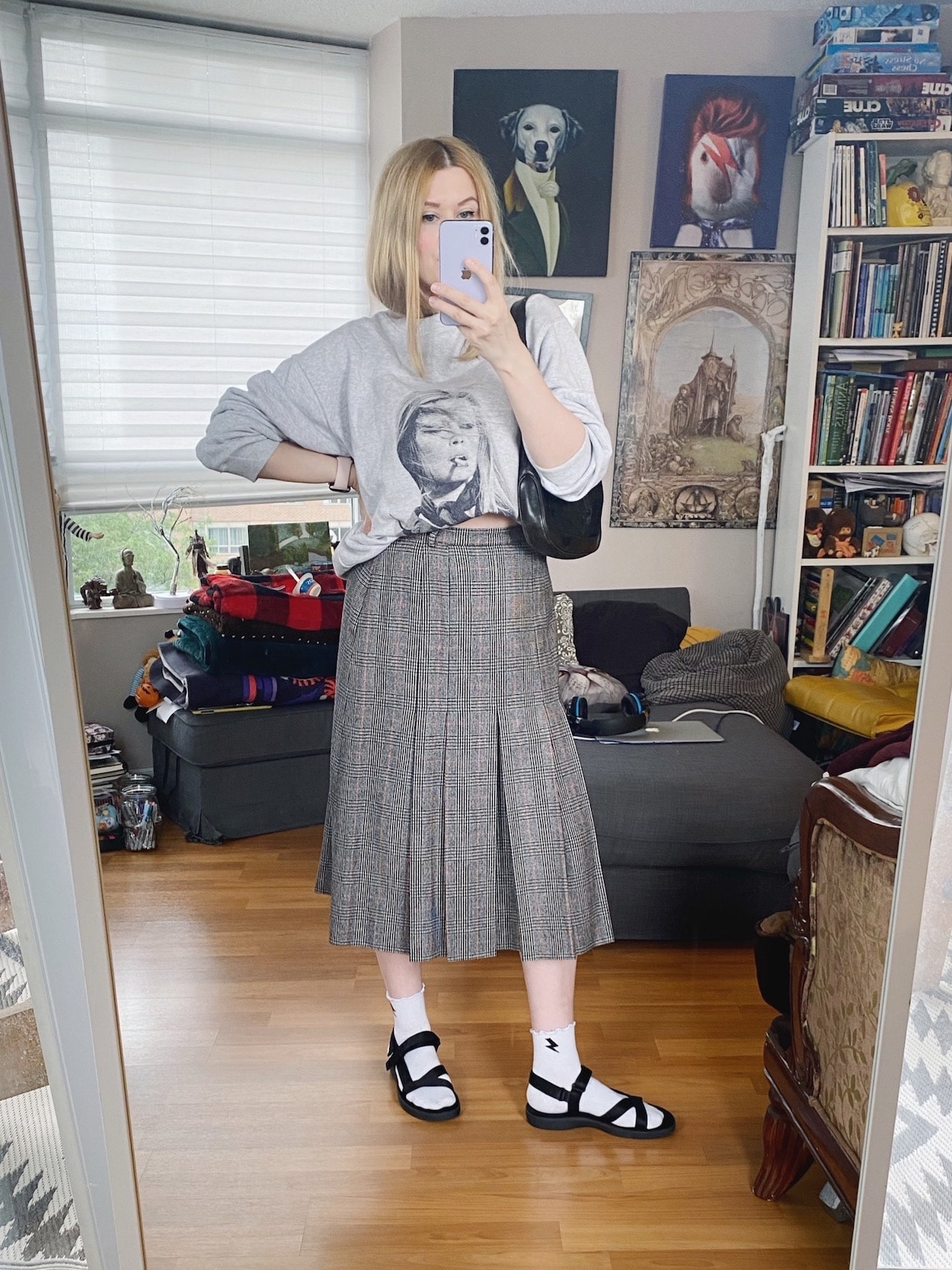 A blonde woman is wearing a vintage plaid skirt, and Anine Bing sweatshirt, sports sandals with socks, and a vintage Gucci bag.