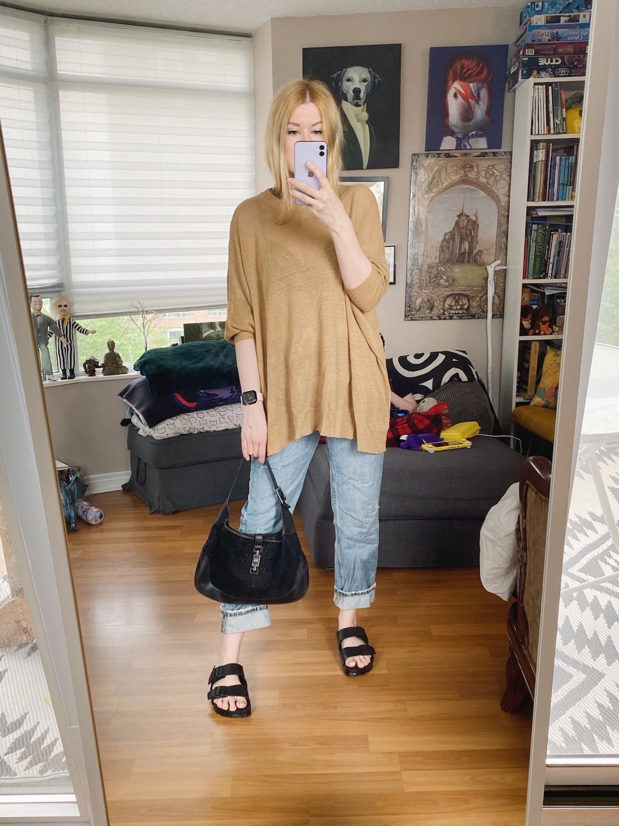 A blonde woman is wearing a linen sweater, boyfriend jeans, Birkenstocks sandals, and a vintage Gucci bag.