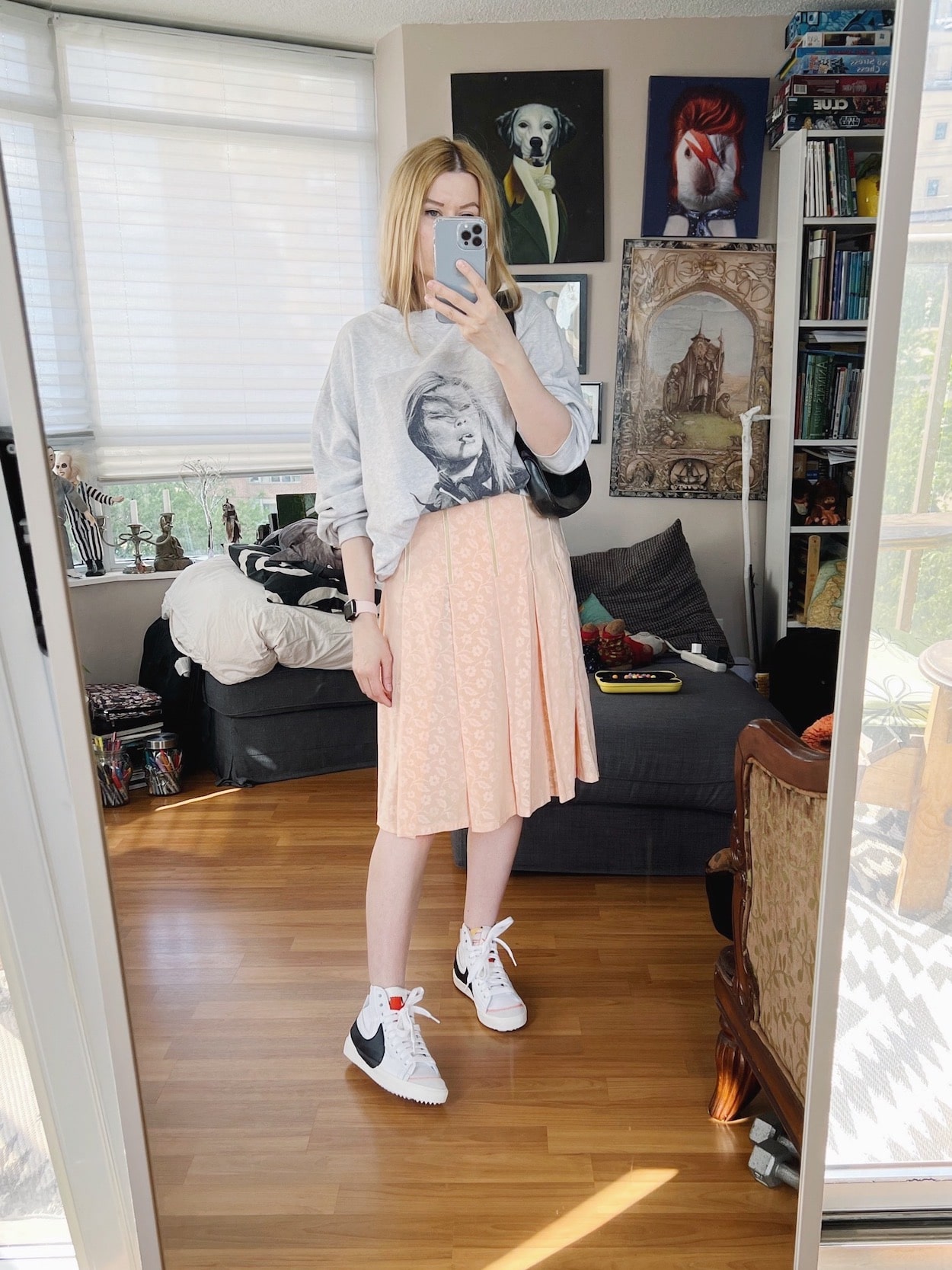 A blonde woman is wearing an Anine Bing sweatshirt, Miu Miu pleated skirt, Nikes, and a vintage Gucci bag.