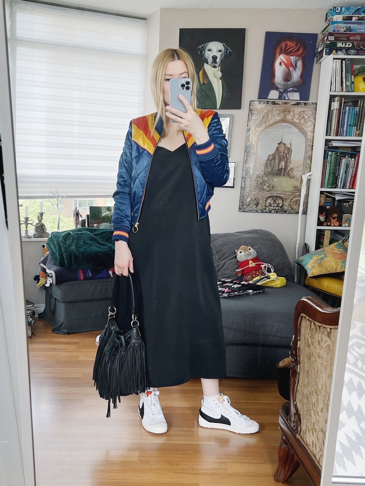 A blonde woman is wearing a slip dress, retro bomber jacket, Nikes, and a vintage bucket bag.