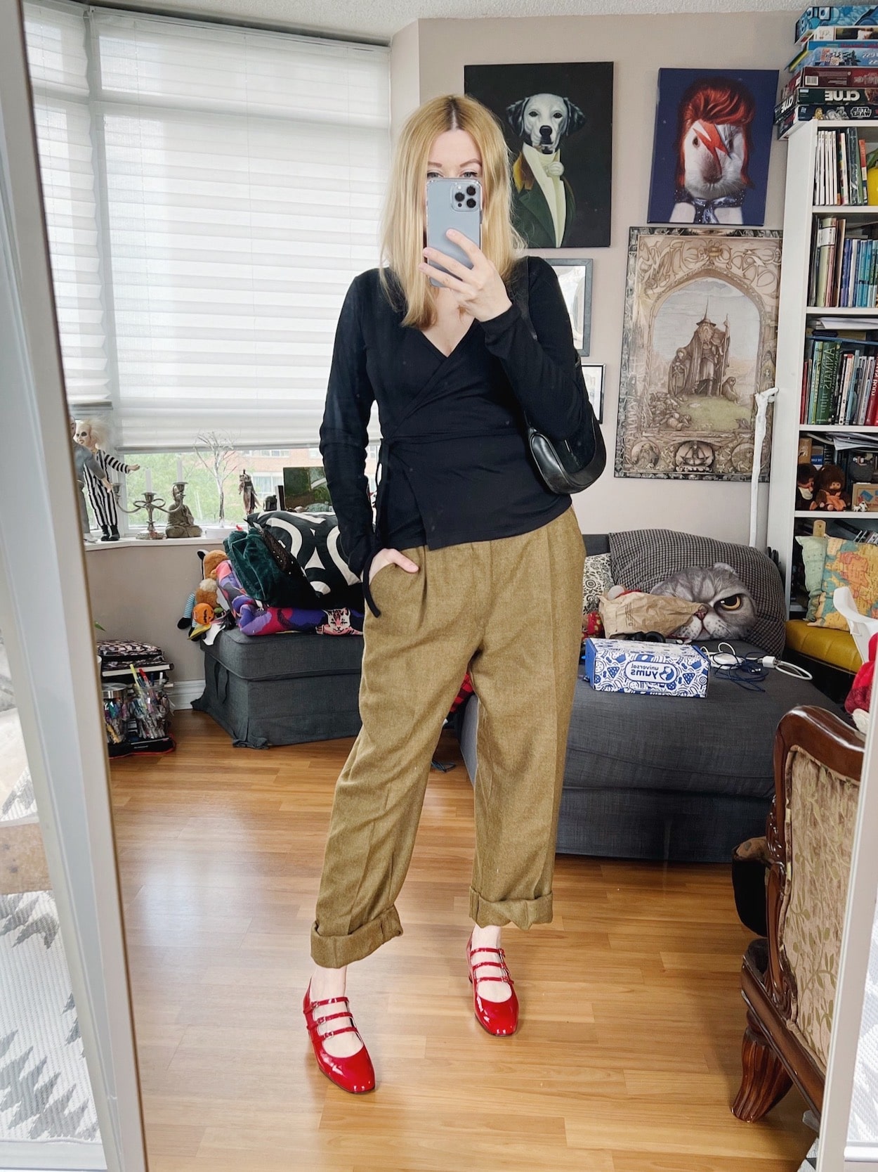 A blonde woman is wearing a black wrap shirt, vintage trousers, red Mary Janes, and a vintage Gucci bag.