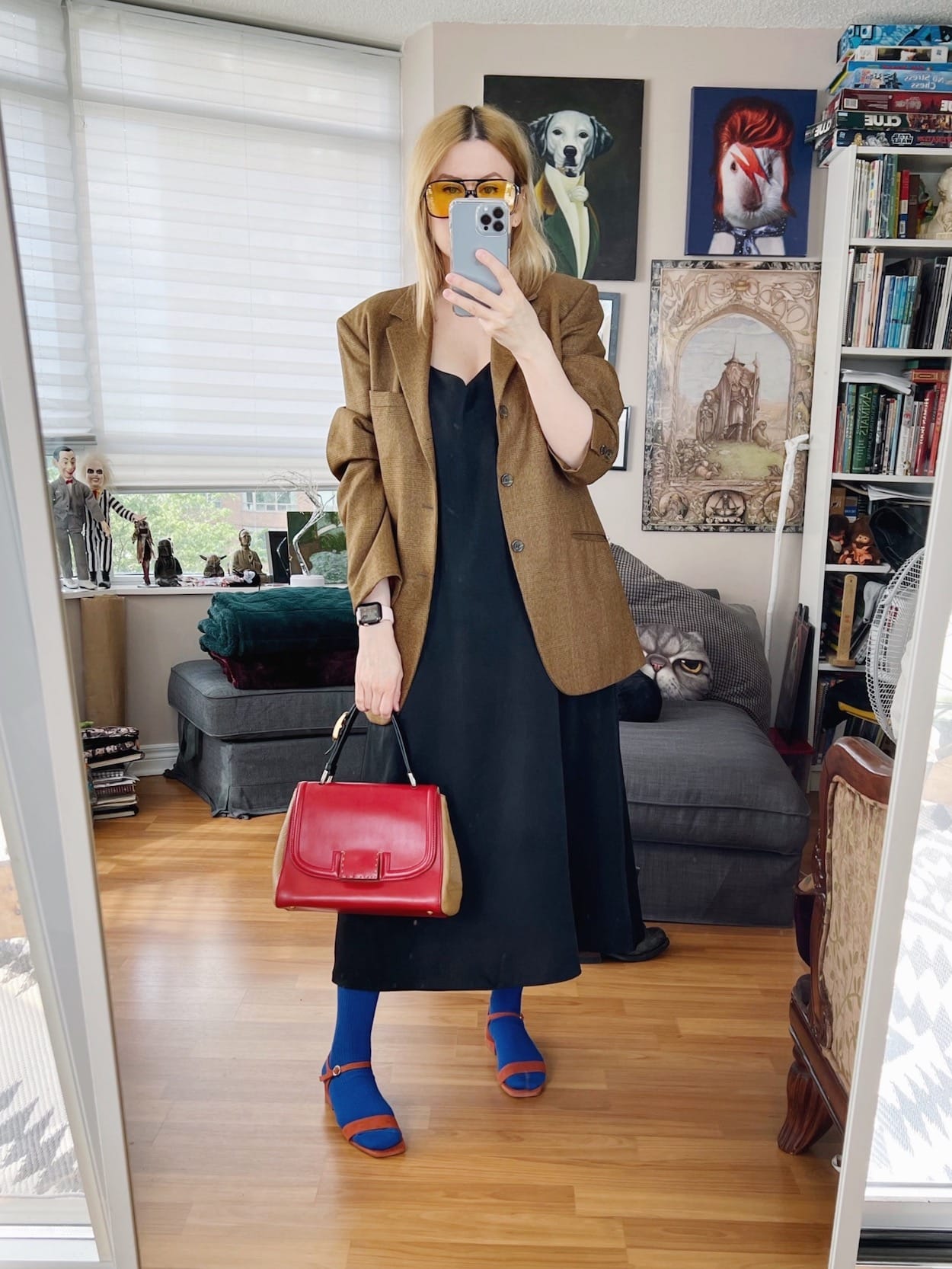 A blonde woman is wearing a black slip dress, oversized blazer, high blue socks with heeled sandals, retro sunglasses, and is carrying a vintage Fendi bag.