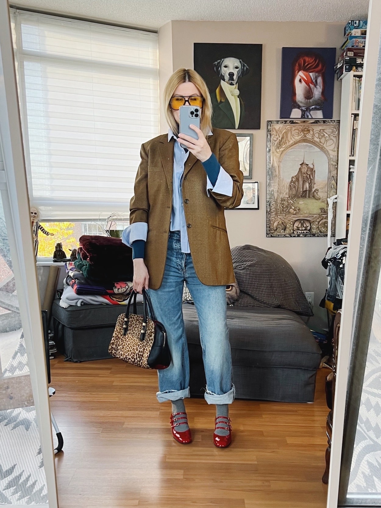 A blonde woman is wearing a roll neck under a button down, under an oversized blazer, with boyfriend jeans, mary janes, retro sunglasses, and an animal print bag.