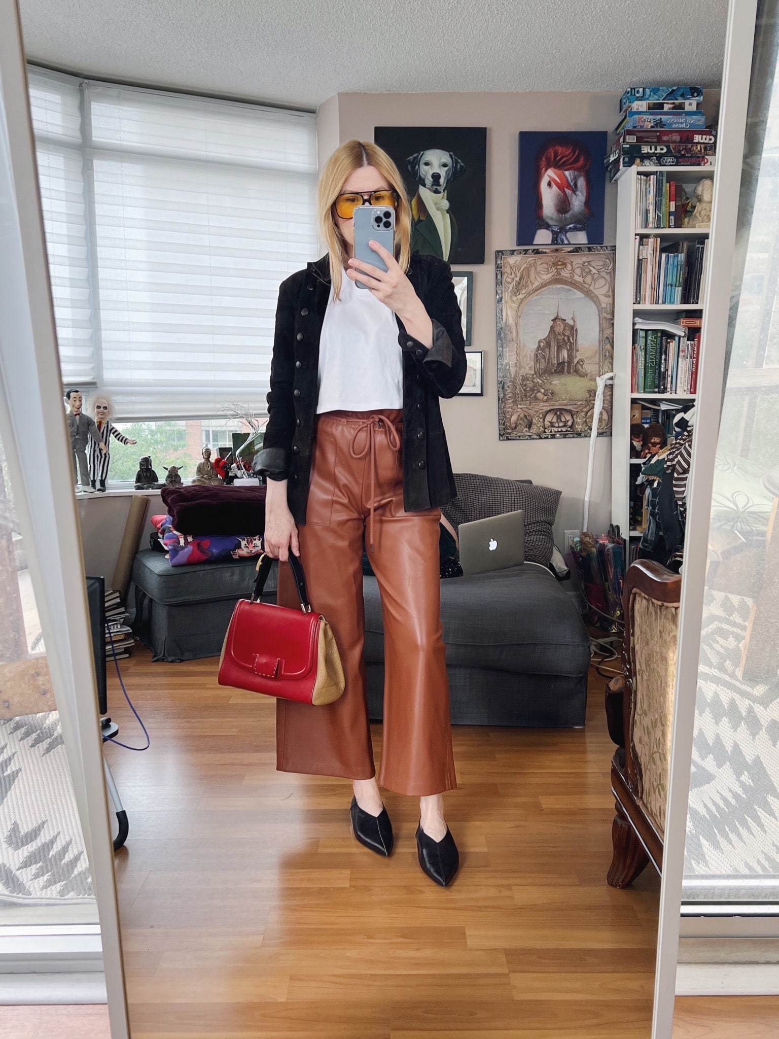 A blonde woman is wearing a cropped tee, brown leather pants, a vintage coat, retro sunglasses, and a vintage Fendi bag.