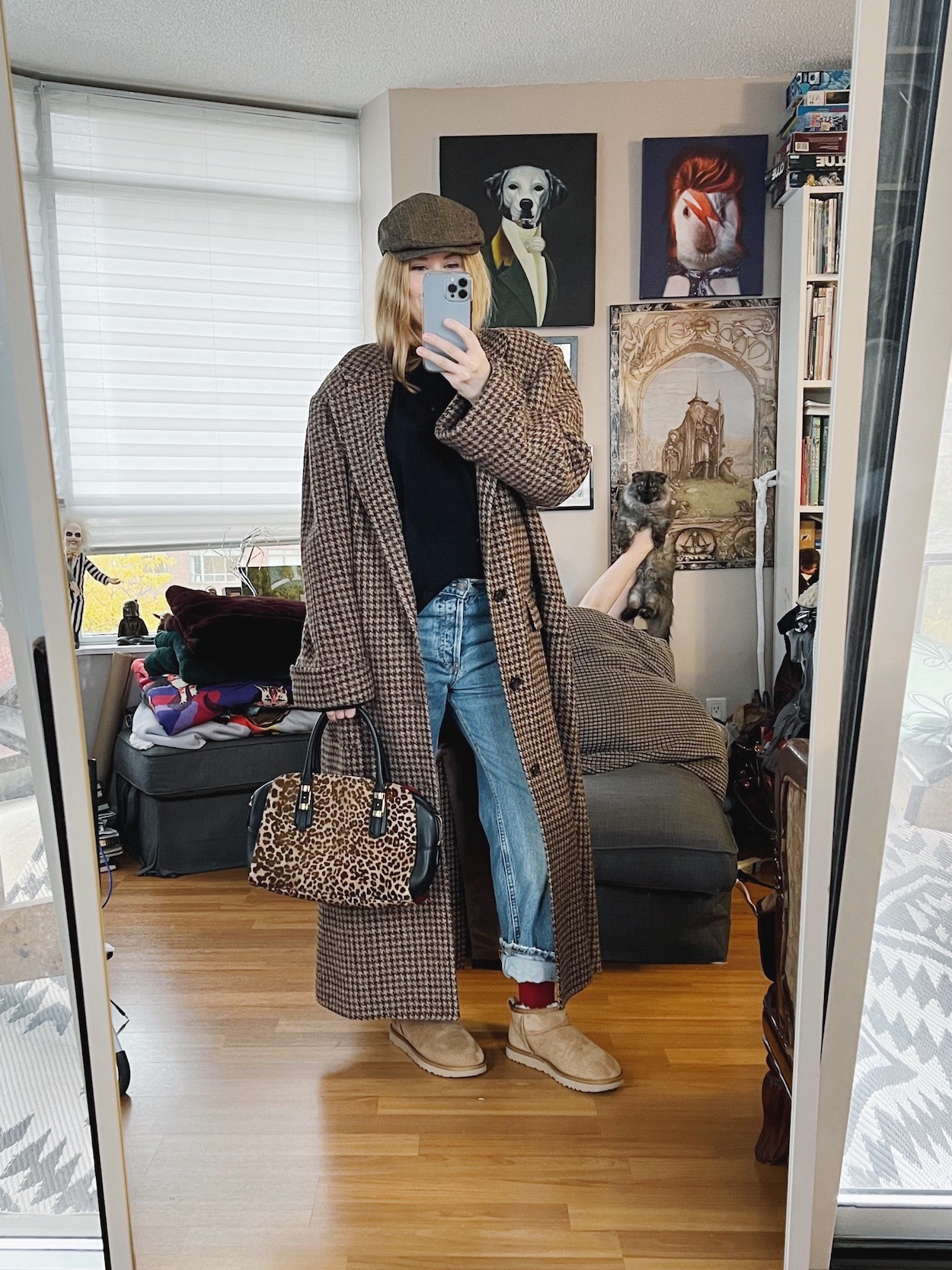 A blonde woman is wearing an oversized vintage Ralph Lauren coat, boyfriend jeans, mini uggs, a cashmere sweater, driving cap, and an animal print handbag.