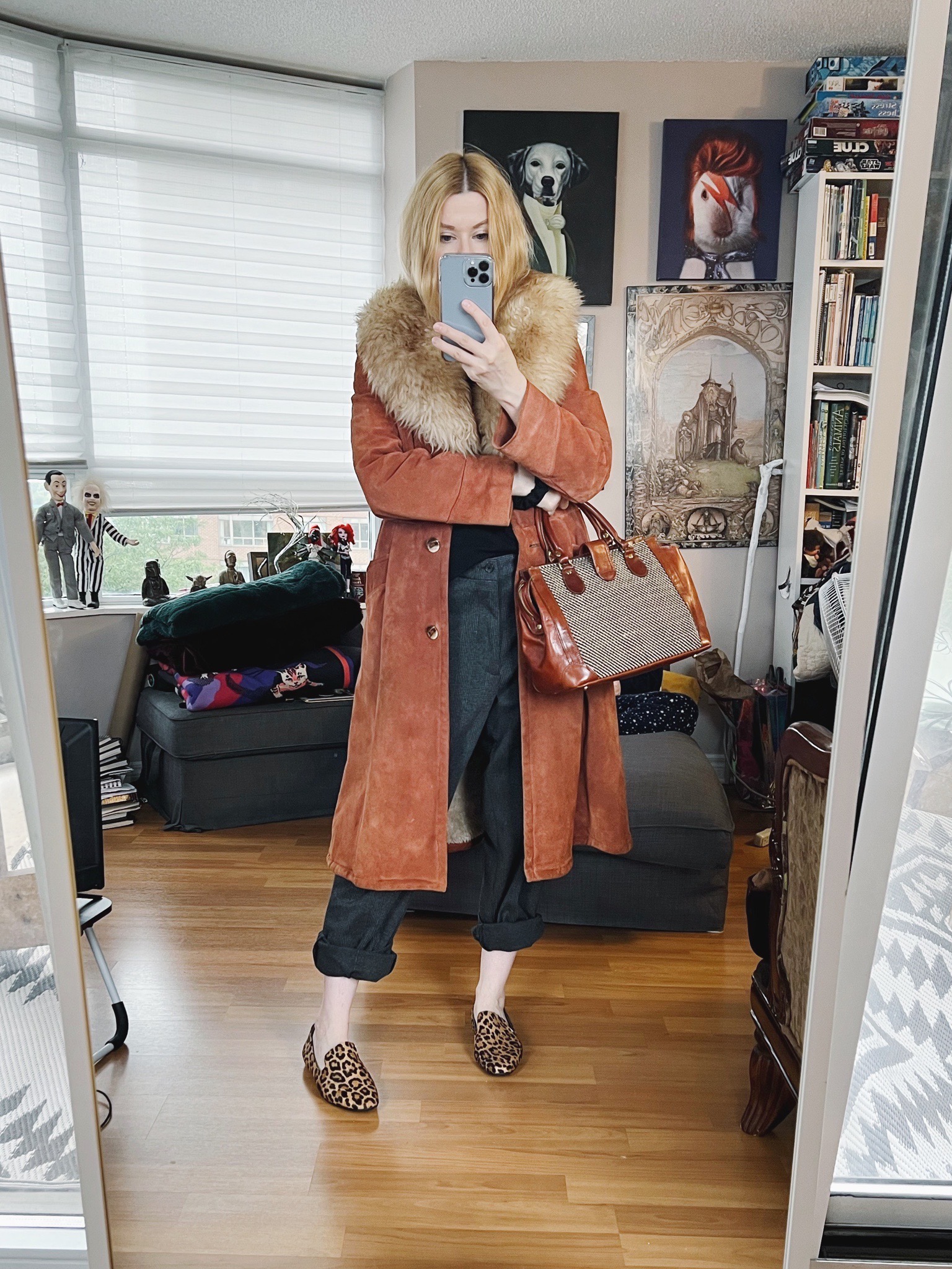 A blonde woman is wearing a vintage jacket, grey trousers, animal print loafers, and is carrying a vintage bag.