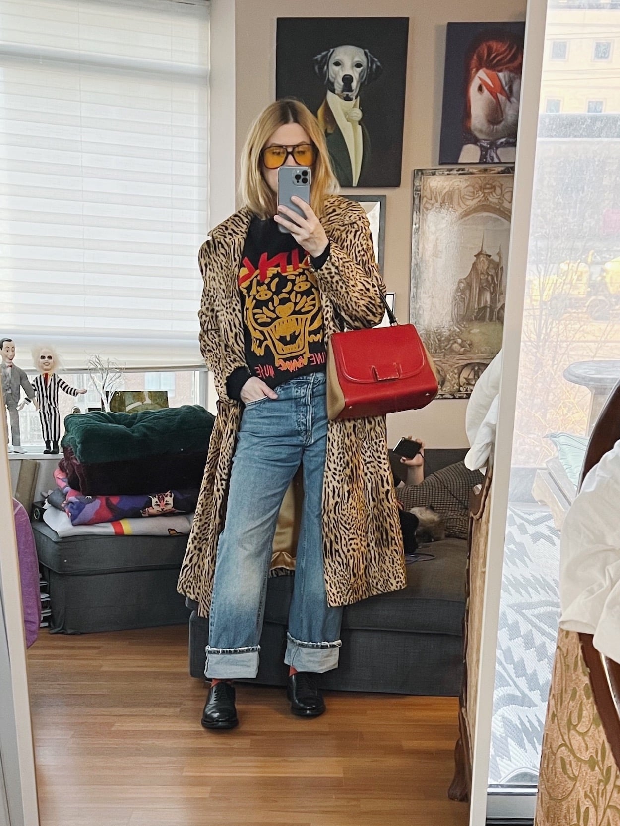 A blonde woman is wearing an animal print coat, Anine Bing sweatshirt, jeans, derby shoes, retro sunglasses, and a vintage Fendi bag.