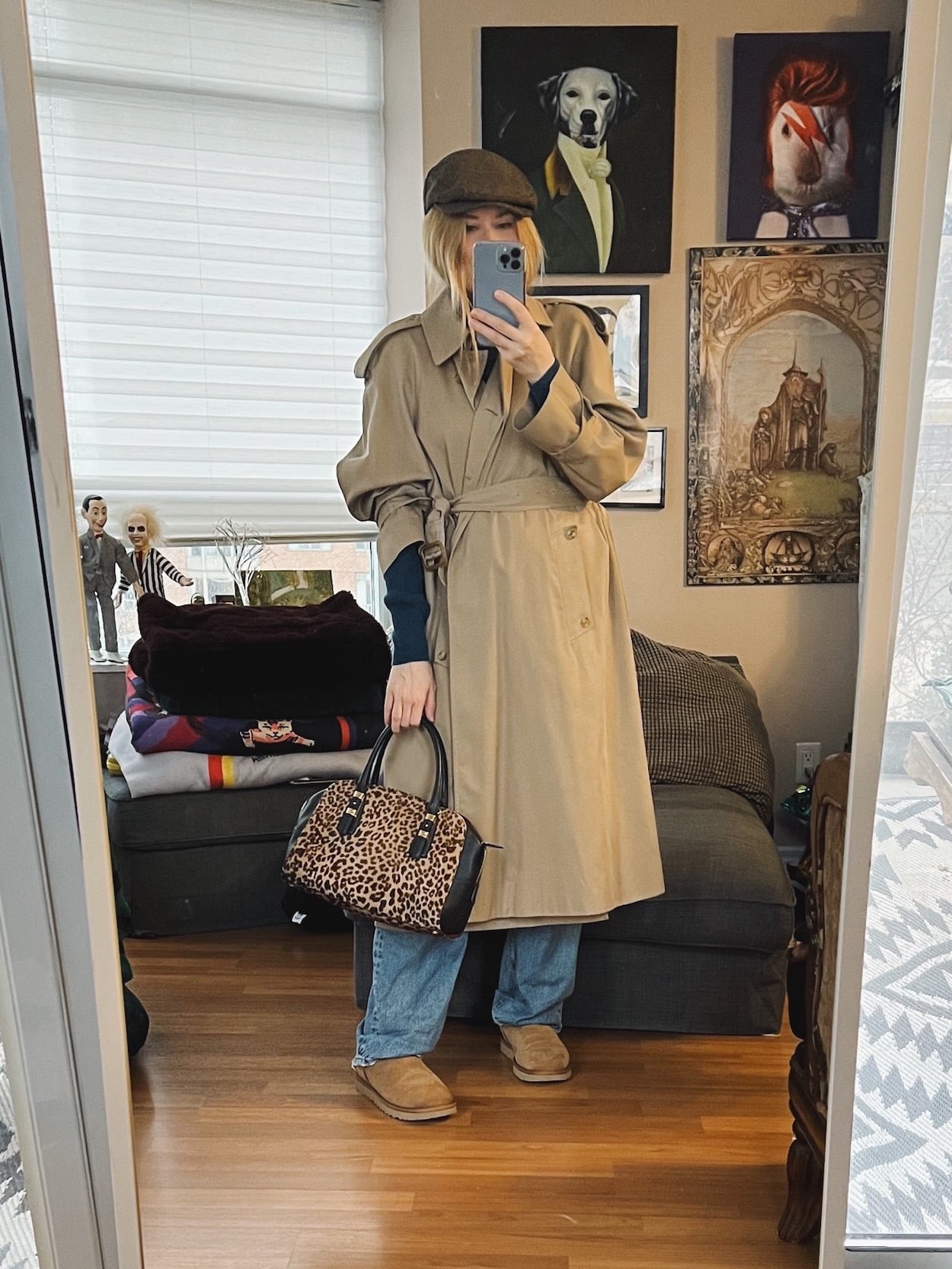 A blonde woman is wearing a vintage trench, jeans, Ugg minis, a driving cap, and an animal print bag.