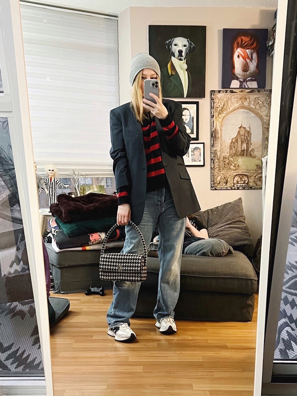 A blonde woman is wearing a striped sweater, navy blue blazer, boyfriend jeans, New Balance sneakers, a grey beanie, and a houndstooth bah.