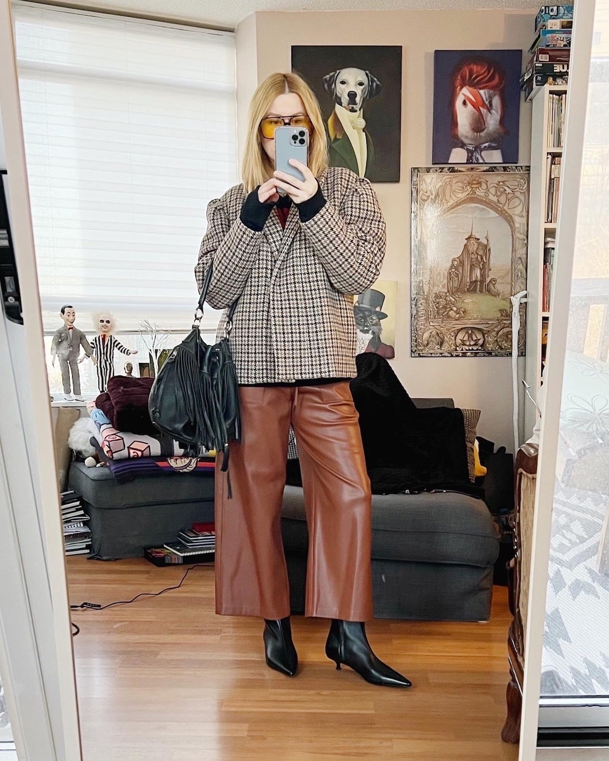 A blonde woman is wearing leather pants, and an oversized plaid blazer, with black boots, a vintage bag, and retro sunglasses.