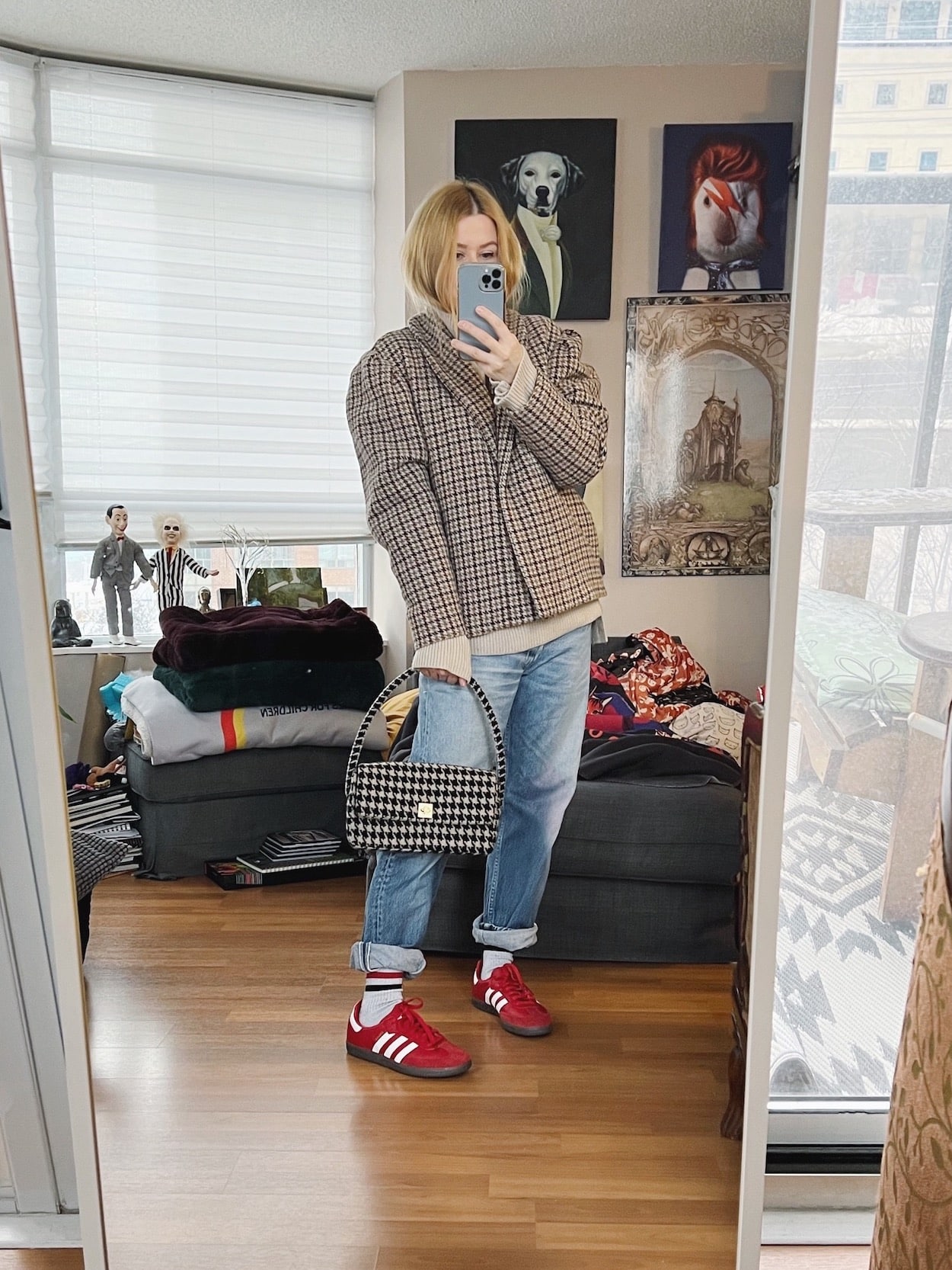 A blonde woman is wearing a houndstooth jacket, boyfriend jeans, red Sambas and a houndstooth bag.