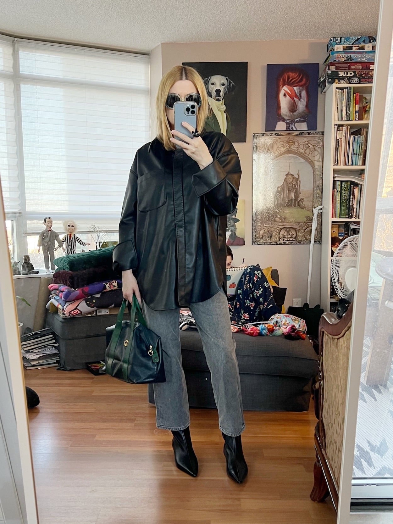 A blonde woman is wearing a faux leather button up, grey jeans, kitten heel boots, vintage sunglasses, and a vintage Longchamp bag.