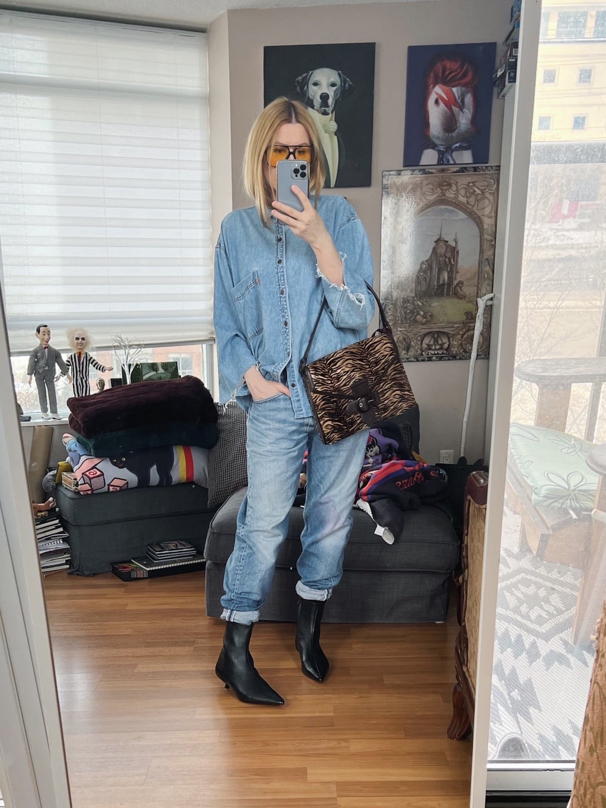 A blonde woman is wearing a double denim outfit, a vintage animal print bag, kitten heel boots, and retro sunglasses.