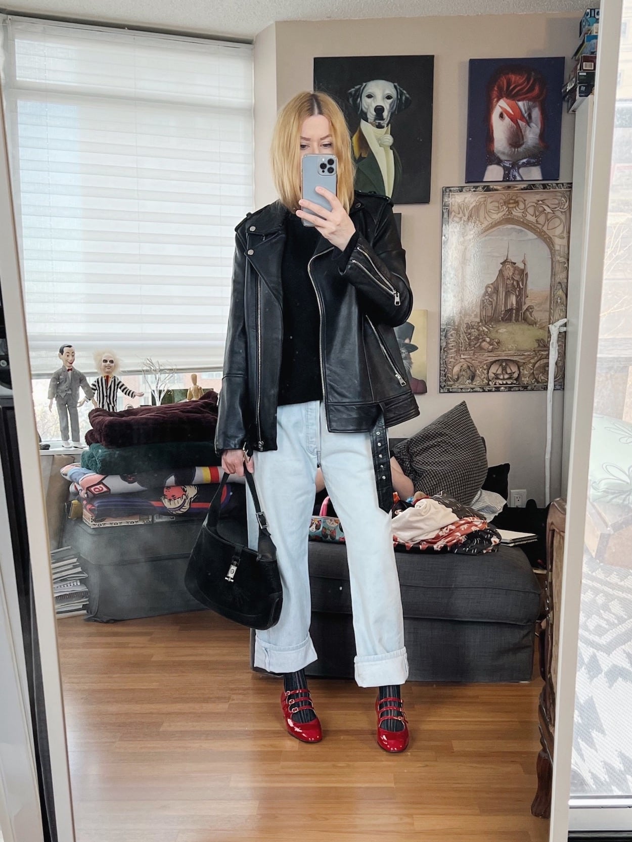 A blonde woman is wearing a black sweater, vintage Levis, an oversized leather jacket, mary janes, and a vintage Gucci bag.