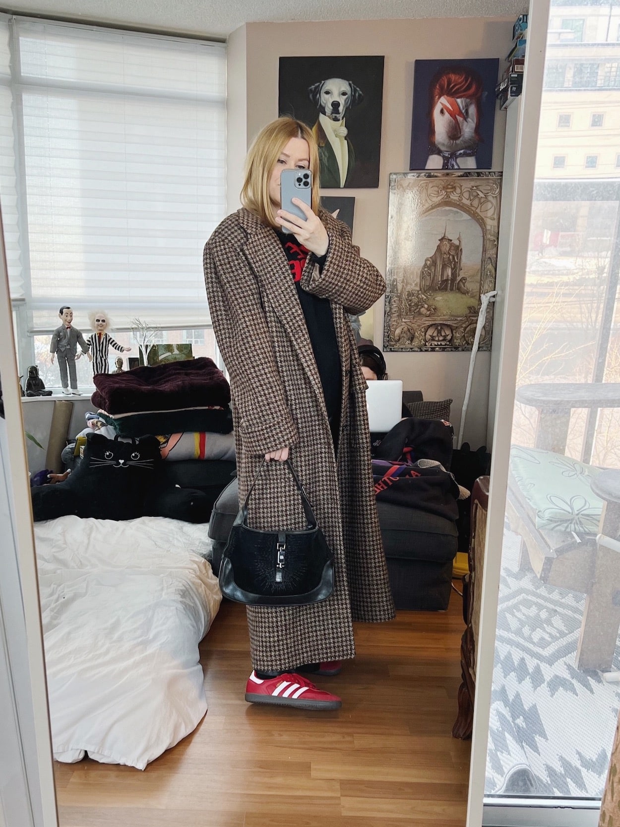 A blonde woman is wearing a Cure sweater, leather pants, and long vintage coat, red Sambas, and a vintage Gucci Jackie bag.
