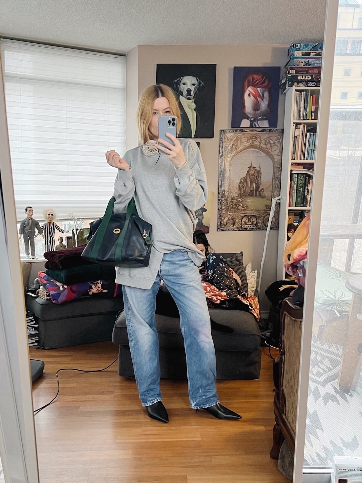 A blonde woman is wearing a grey sweatshirt, vintage Levi's, kitten heel boots, and carrying a vintage Longchamp bag.