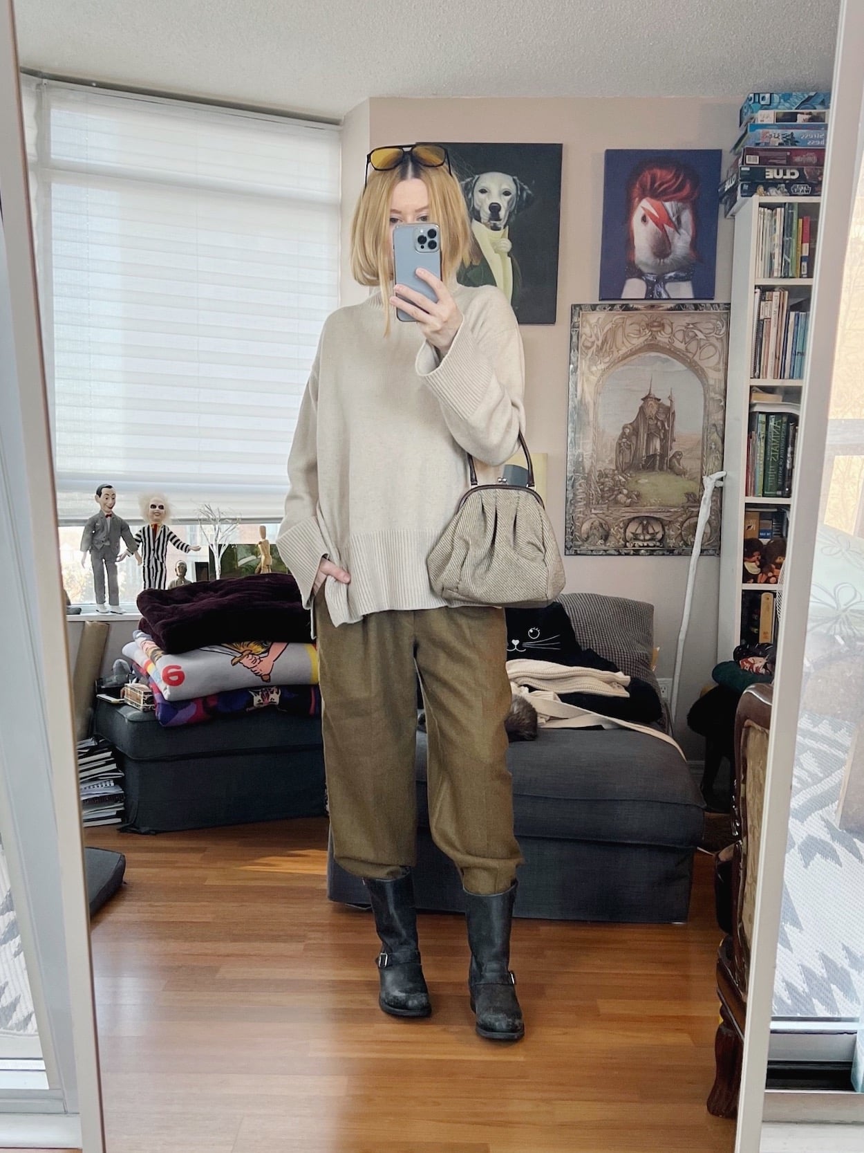 A blonde woman is wearing an oversized sweater, vintage trousers, Frye boots, and a vintage Miu Miu bag.