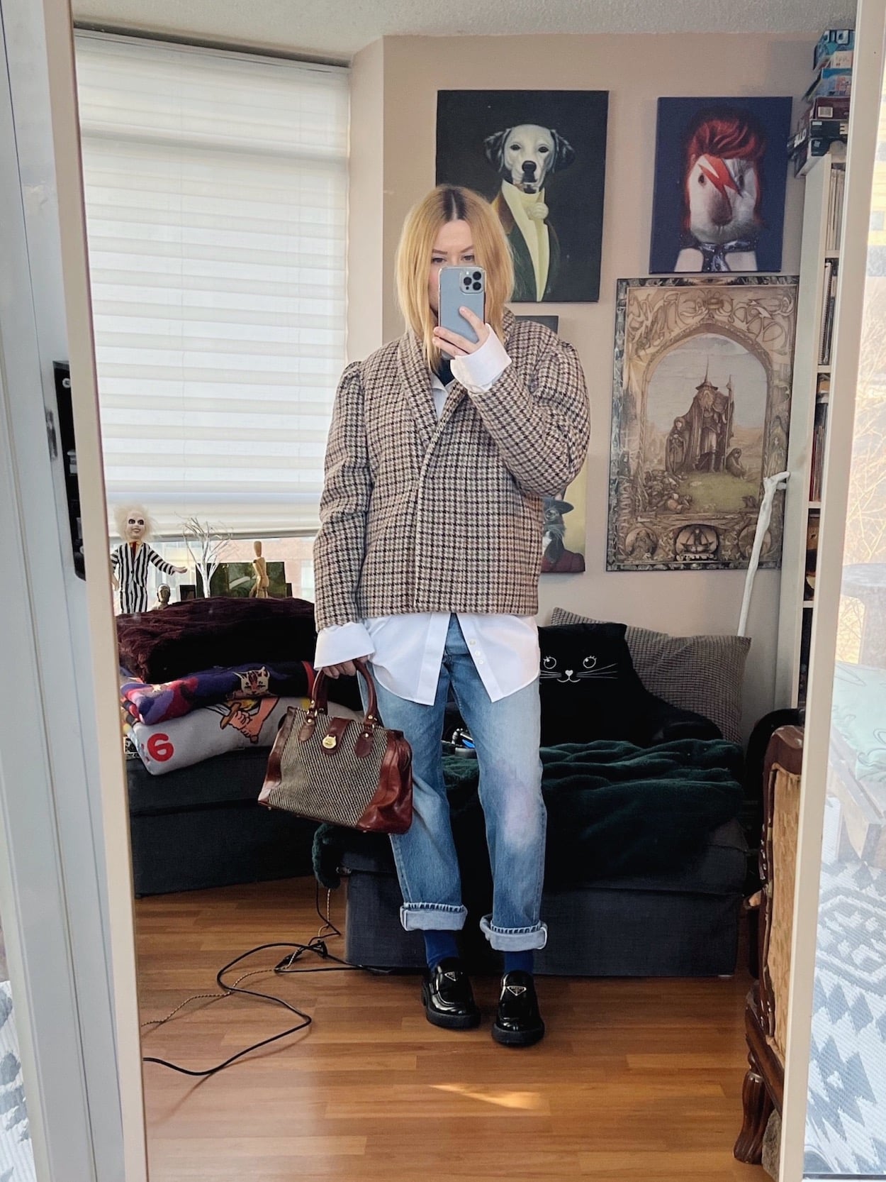 A blonde woman is wearing vintage Levis, a button up, herringbone jacket, Prada loafers, and a vintage handbag.