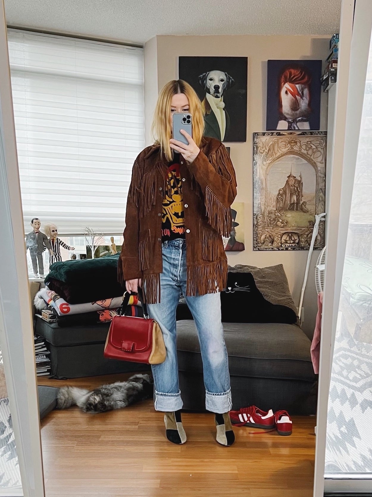 A blonde woman is wearing a vintage fringe jacket, sweatshirt, vintage Levi's, patch boots, and a Fendi bag.