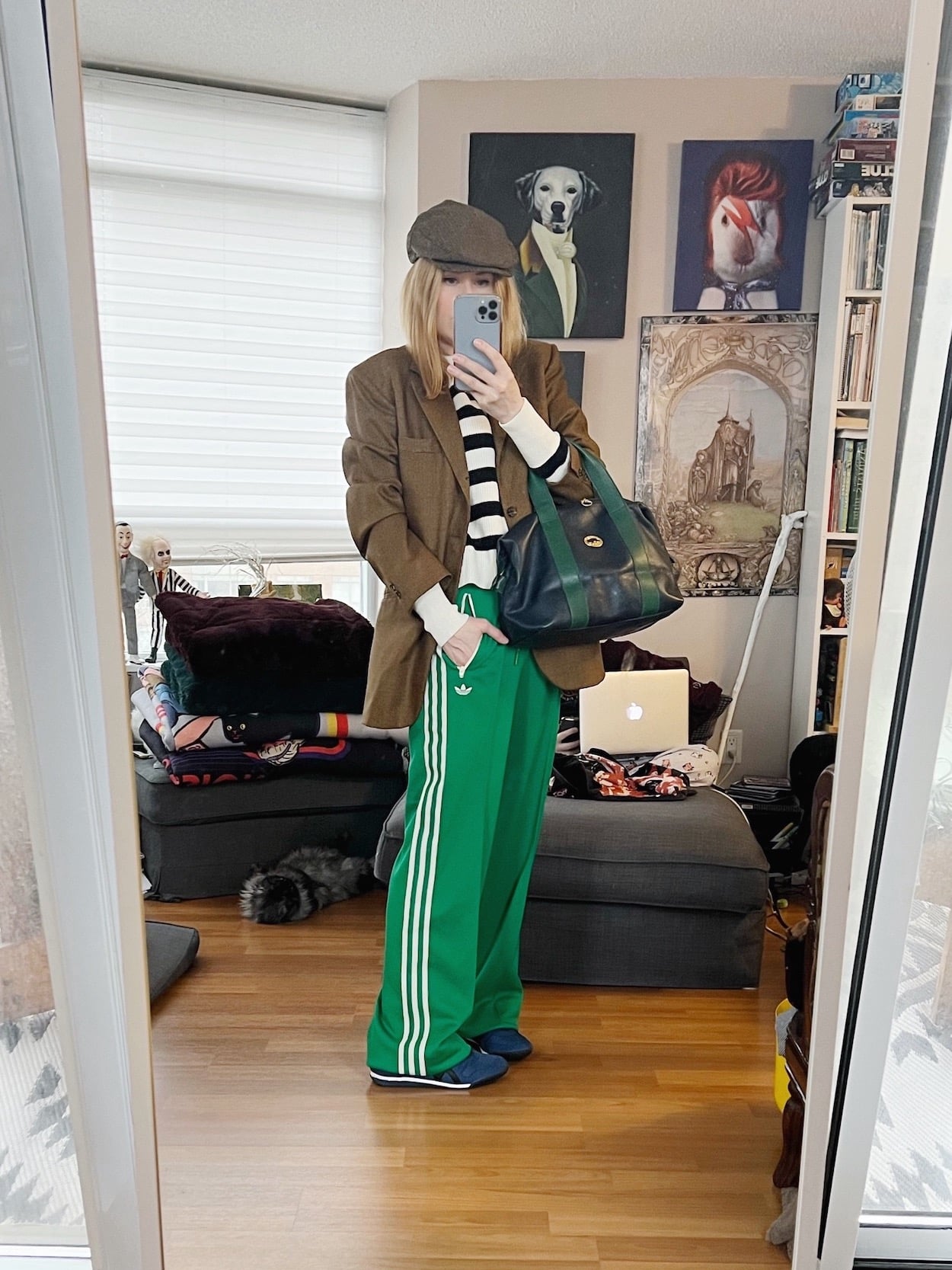 A blonde woman is wearing a striped sweater, vintage blazer, green Adidas pants, a driving cap, Onitsuka Tiger sneakers, and a vintage Longchamp bag.