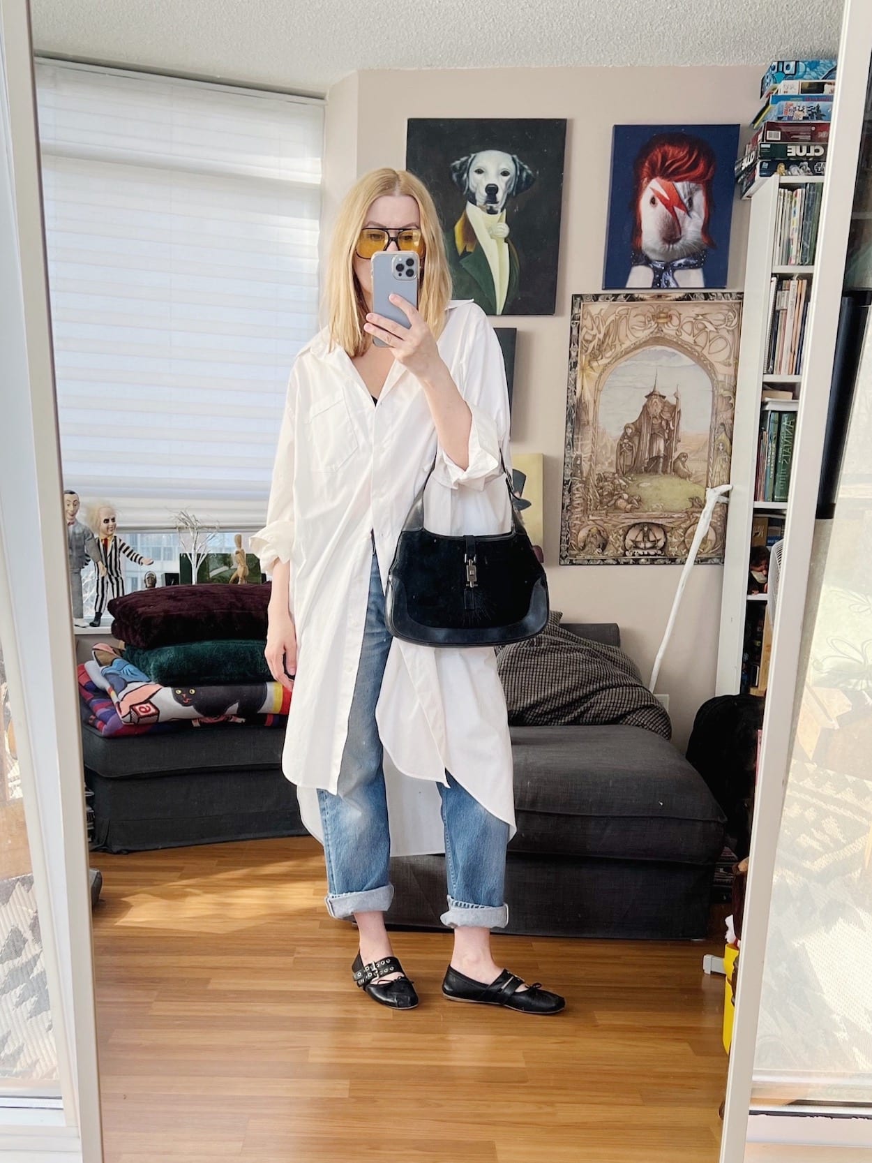 A blonde woman is wearing a way oversized white button up, vintage Levi's, retro sunglasses, Miu Miu ballet flats, and a vintage Gucci bag.