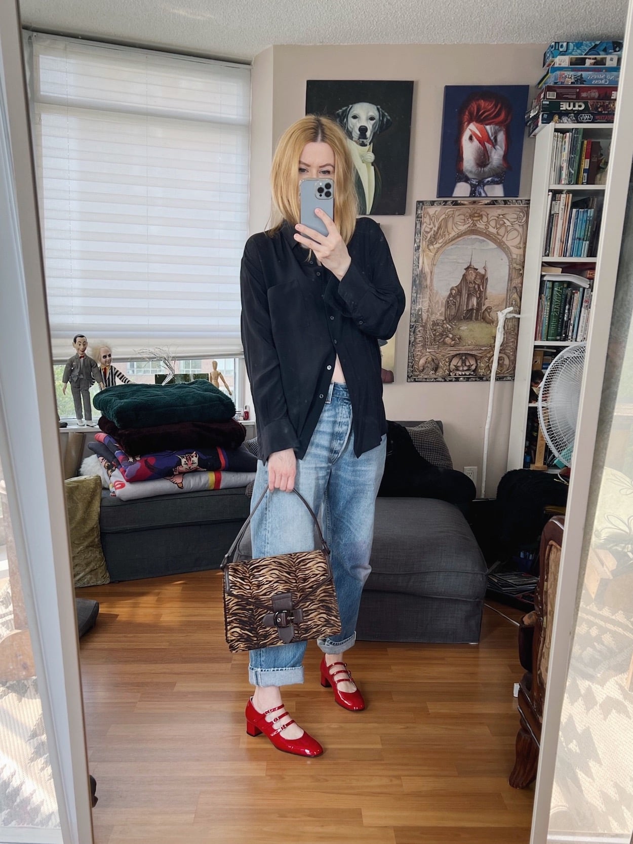 A blonde woman is wearing a black silk blouse, vintage Levi's, red Mary Jane's, and a vintage animal print bag.