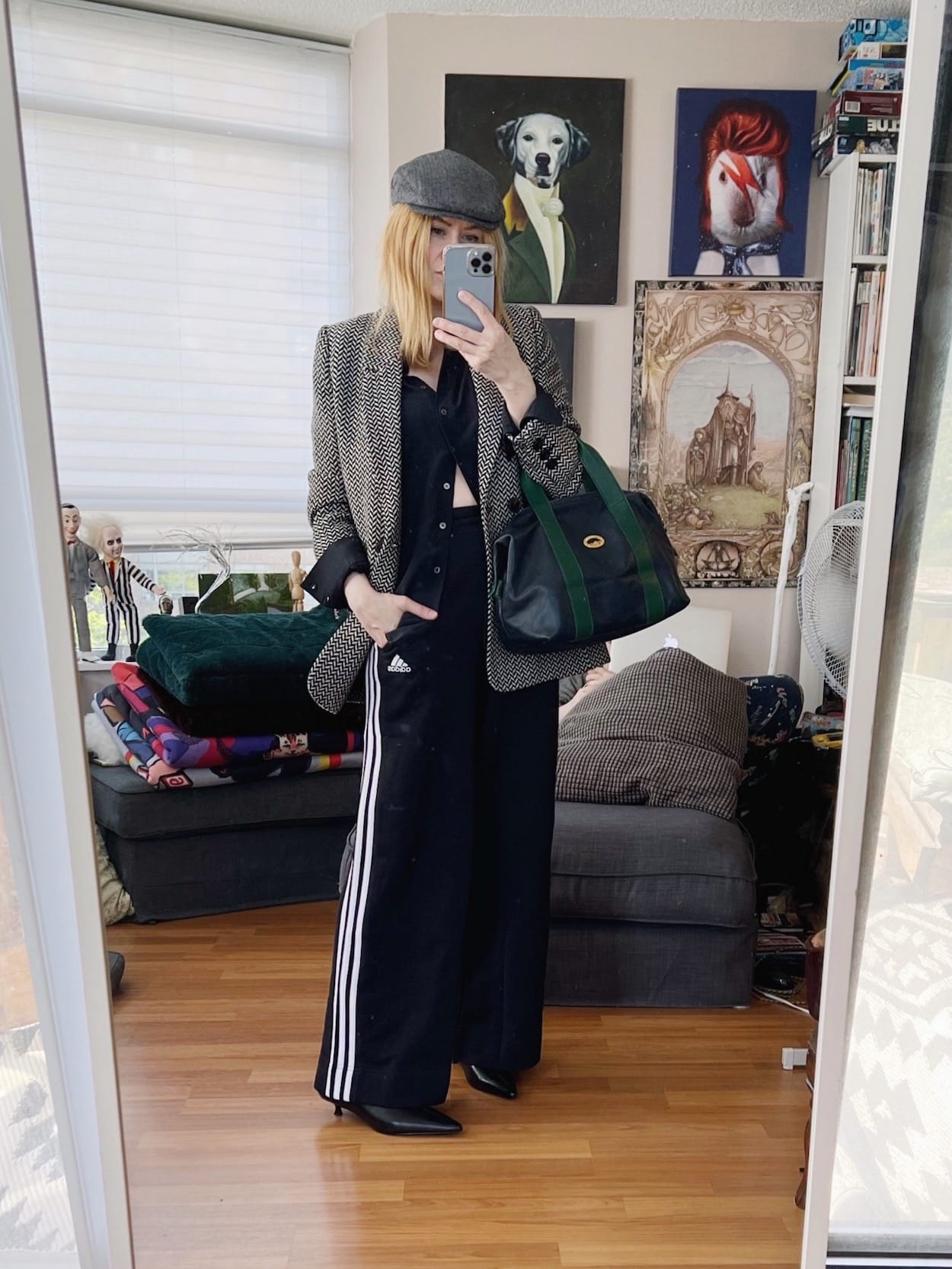 A blonde woman is wearing a silk blouse, blazer, Adidas track pants, hat, black boots, and a vintage bag.