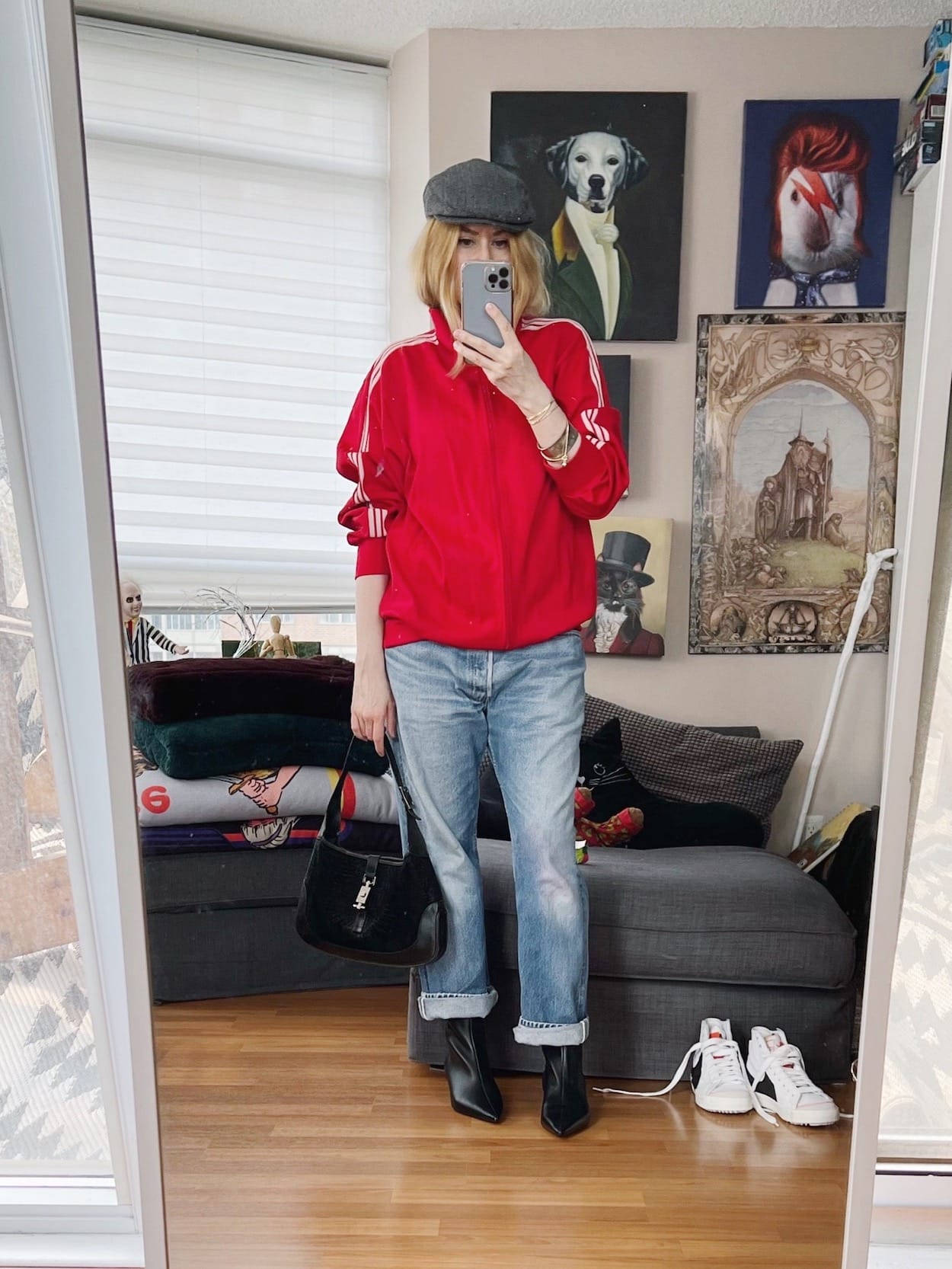 A blonde woman is wearing a vintage Adidas track jacket, vintage jeans, boots, a hat, and a vintage Gucci bag.