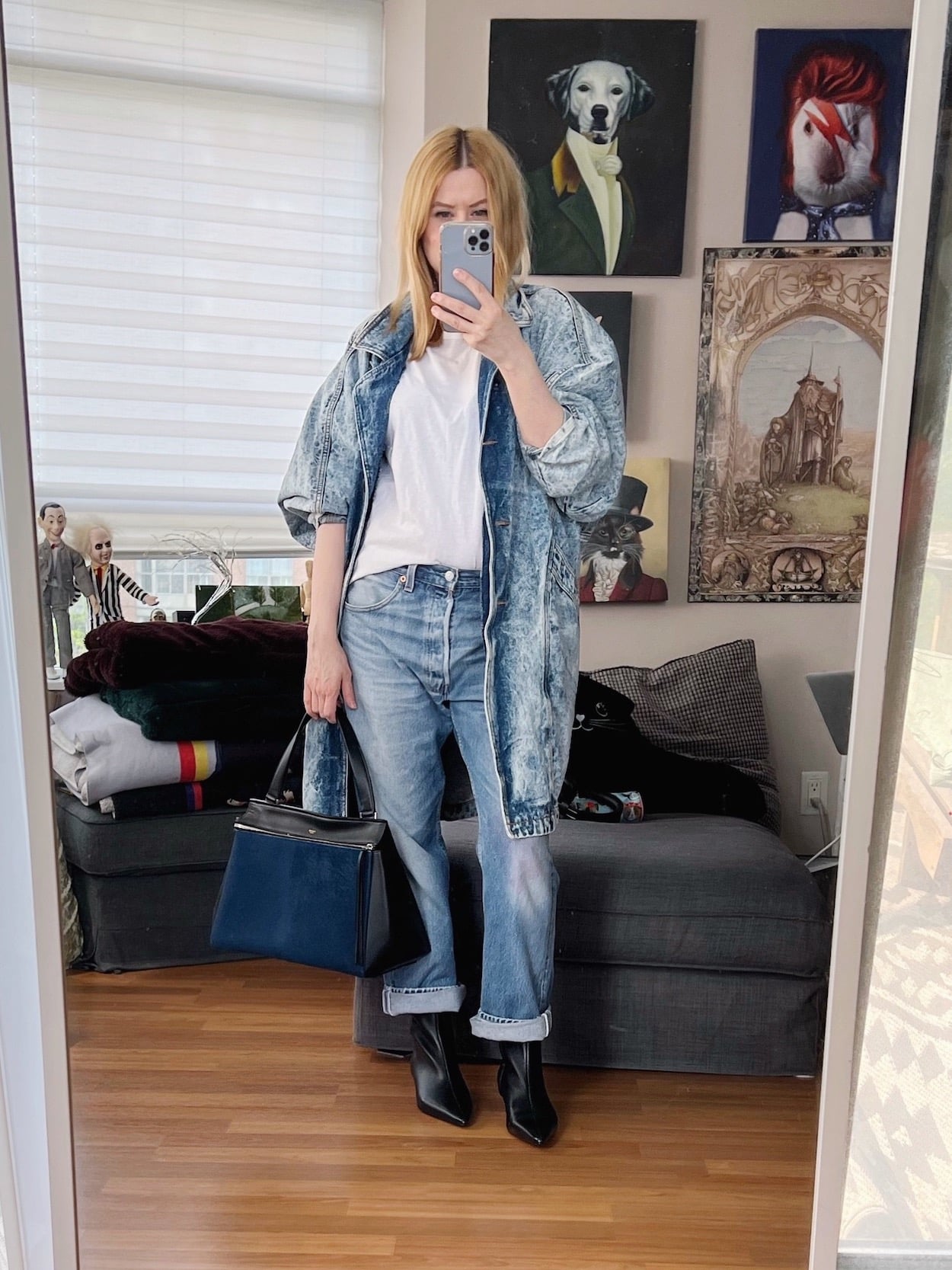 A blonde woman is wearing a white tee, vintage jeans, vintage denim jacket, boots, and a Celine Edge bag.