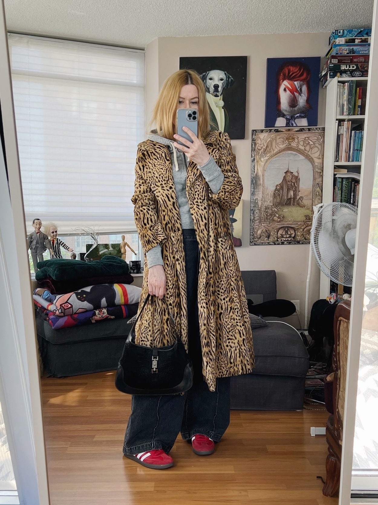 A blonde woman is wearing a grey hoodie, black jeans, a vintage animal print coat, sneakers, and a Celine bag.