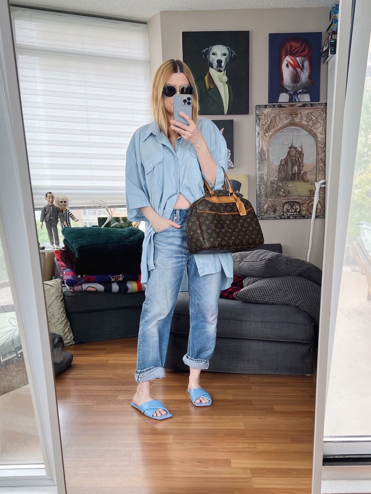 A blonde woman is wearing an oversized button up, vintage Levis, blue sandals, vintage sunglasses, and a vintage Louis Vuitton bag.